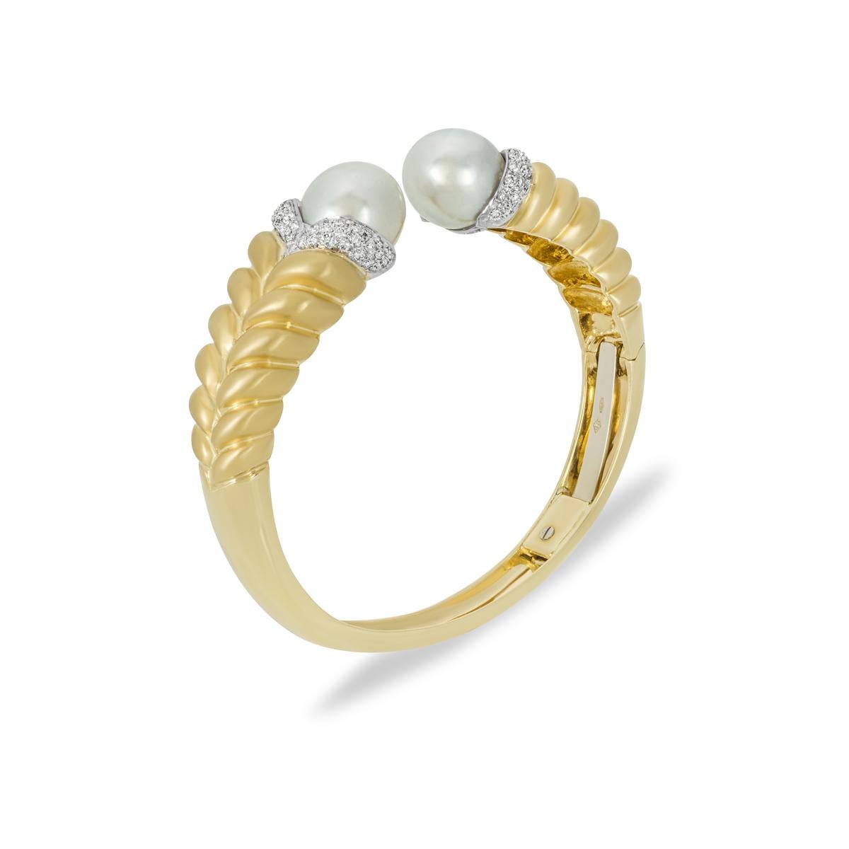 A demure 18k yellow gold pearl and diamond cuff bangle. Two white pearls adorn the terminations measuring 12mm wide and accented by pave set diamonds. The 84 round brilliant cut diamonds have an approximate total weight of 0.92ct, F-G colour and SI