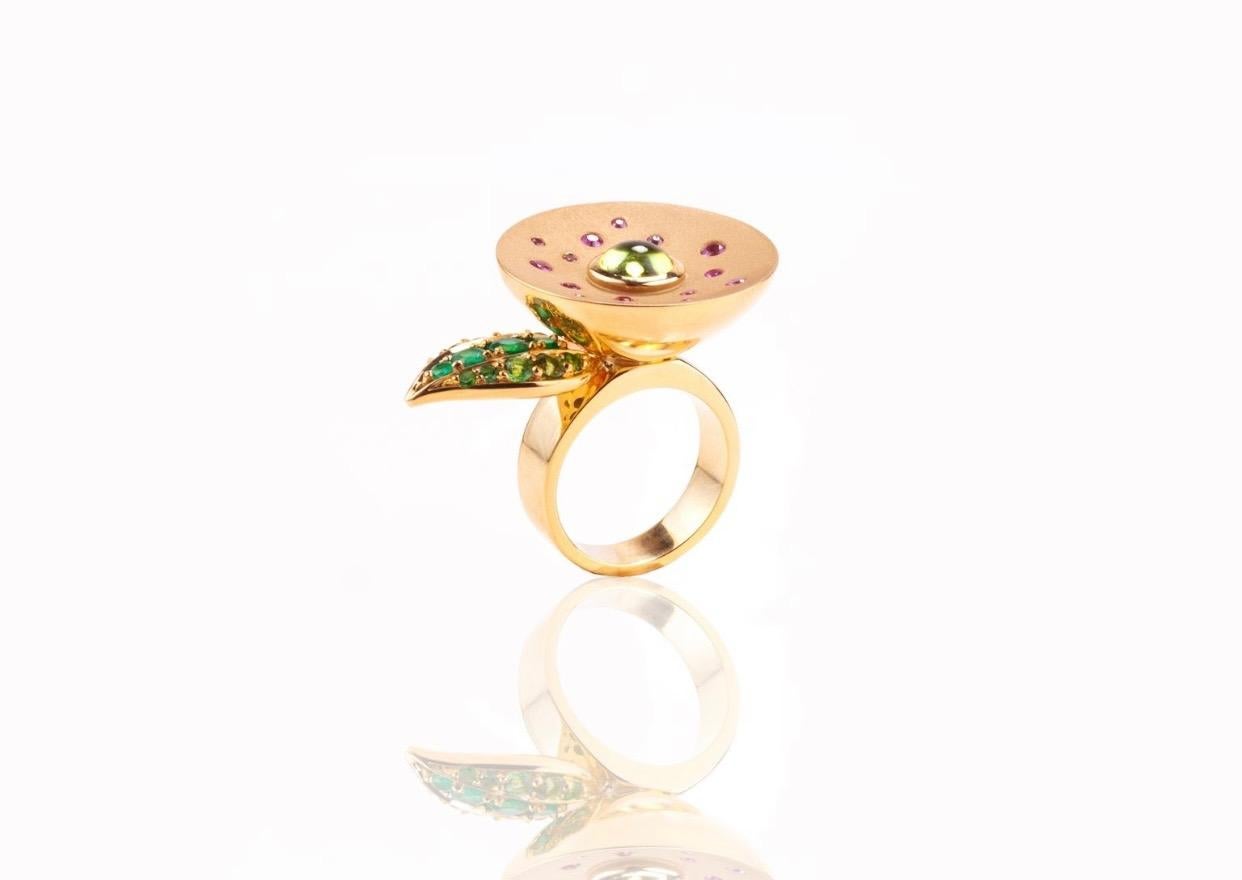 Hand made in 18 karat yellow gold with one Peridot cabochon in the centre, 15 brilliant cut Pink Sapphires which make the flower on a brushed gold inverted dome; 9 brilliant cut Tsavorites and 4 brilliant cut Emeralds make the leaf on the side