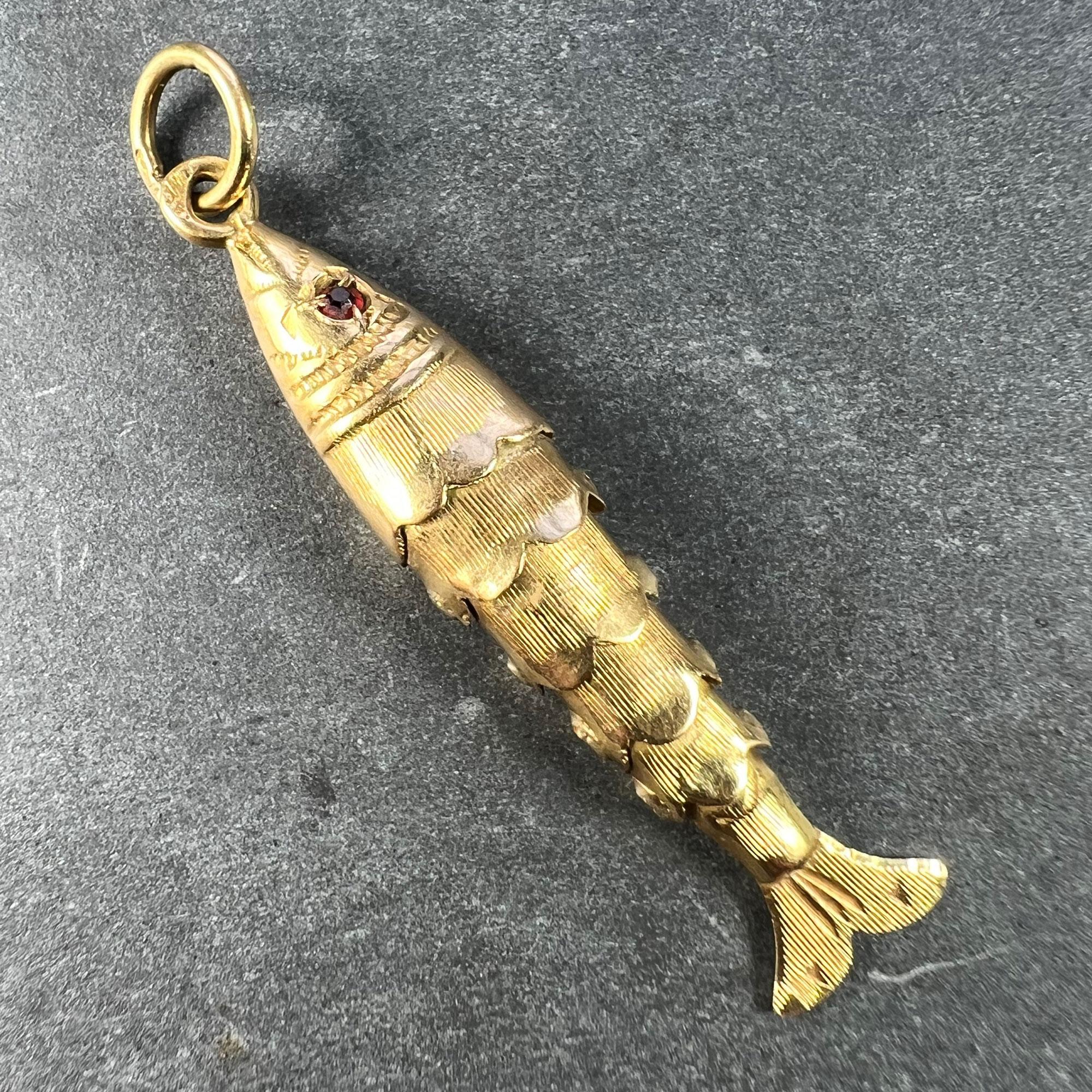 An 18 karat (18K) yellow gold charm pendant designed as an engraved articulated fish with moving body and tail, the eyes each set with a round cut red paste stone. Stamped with a French import head for 18 karat gold.

Dimensions: 3 x 0.7 x 0.45 cm