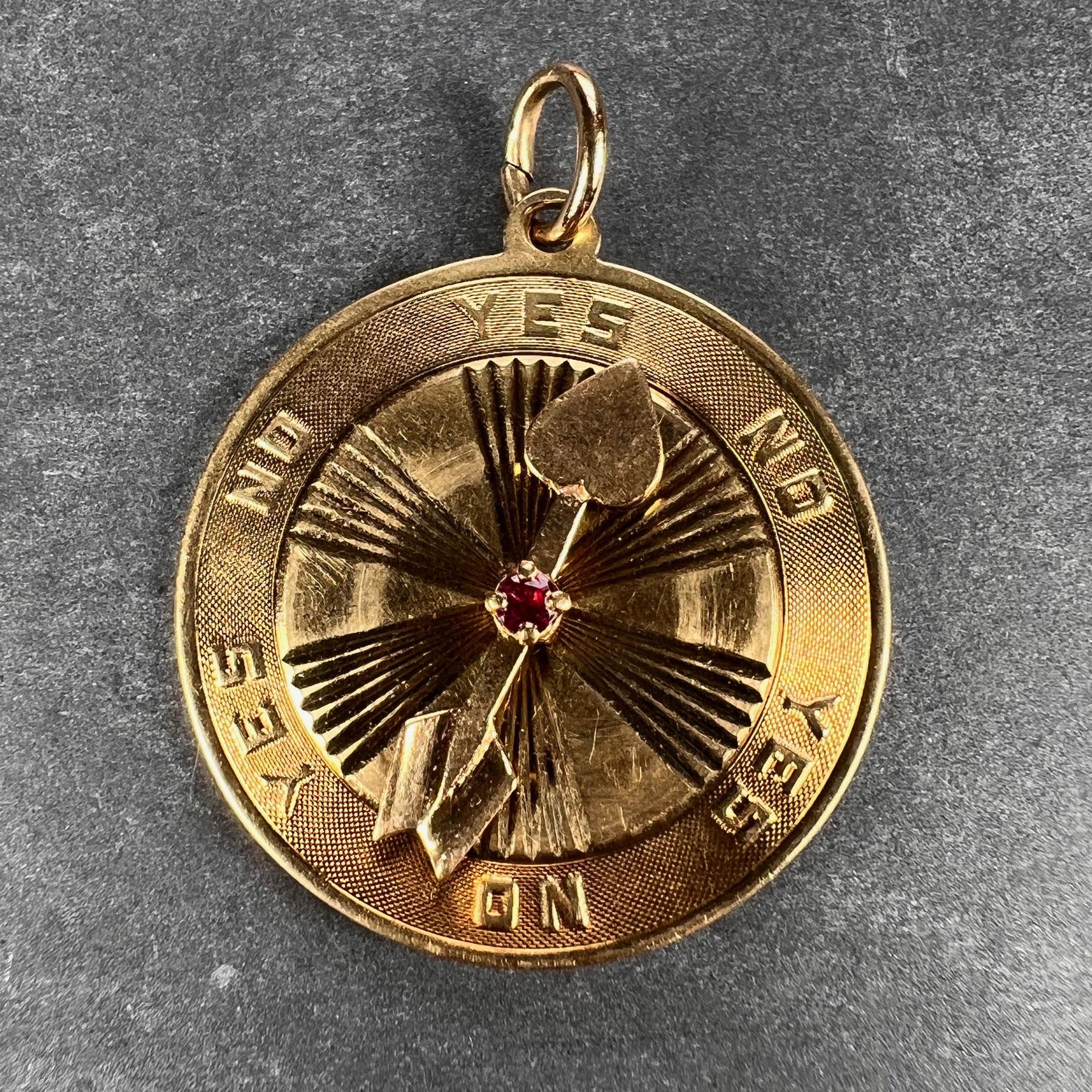 A 14 karat yellow gold charm pendant designed as a disc with yes / no options and a spinning arrow with heart tip and red ruby centre to help make decisions in love. Stamped 14K for 14 karat gold and American manufacture.

Dimensions: 3.2 x 2.6