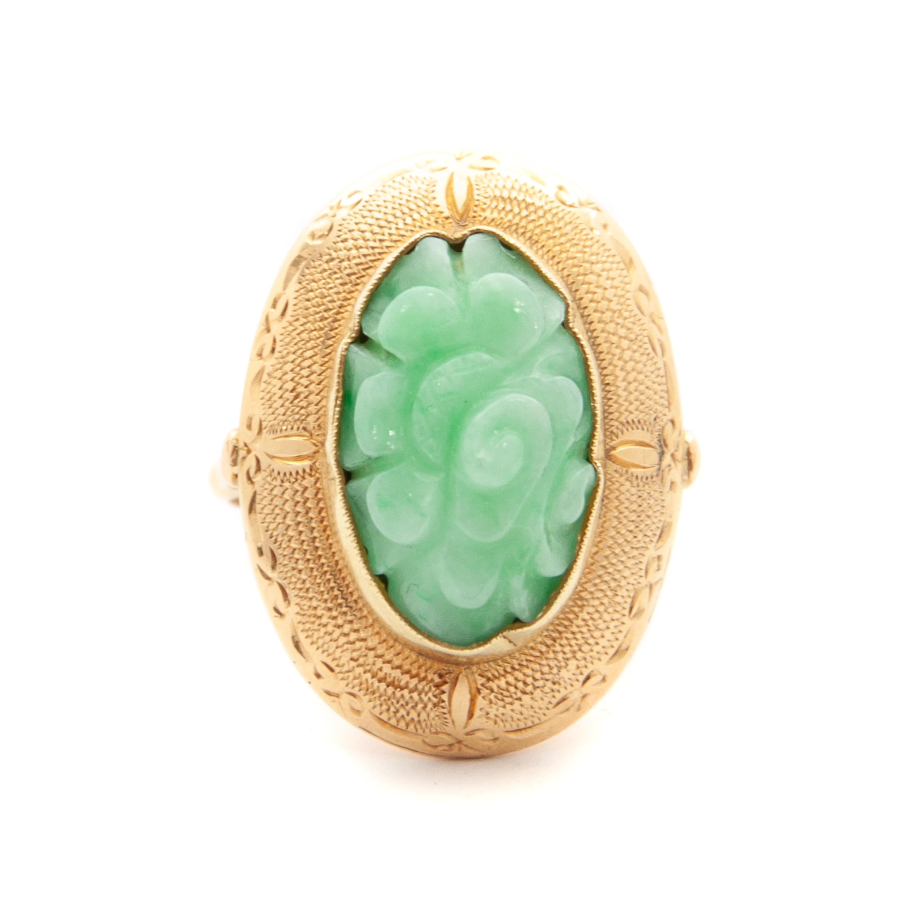 This beautiful vintage oval-shaped 14 karat gold ring is set with a floral carved apple green jade stone. The gold of this beautiful jade ring is accentuated by a matte satin etched design. The gold frame is very nicely decorated with a raised edge