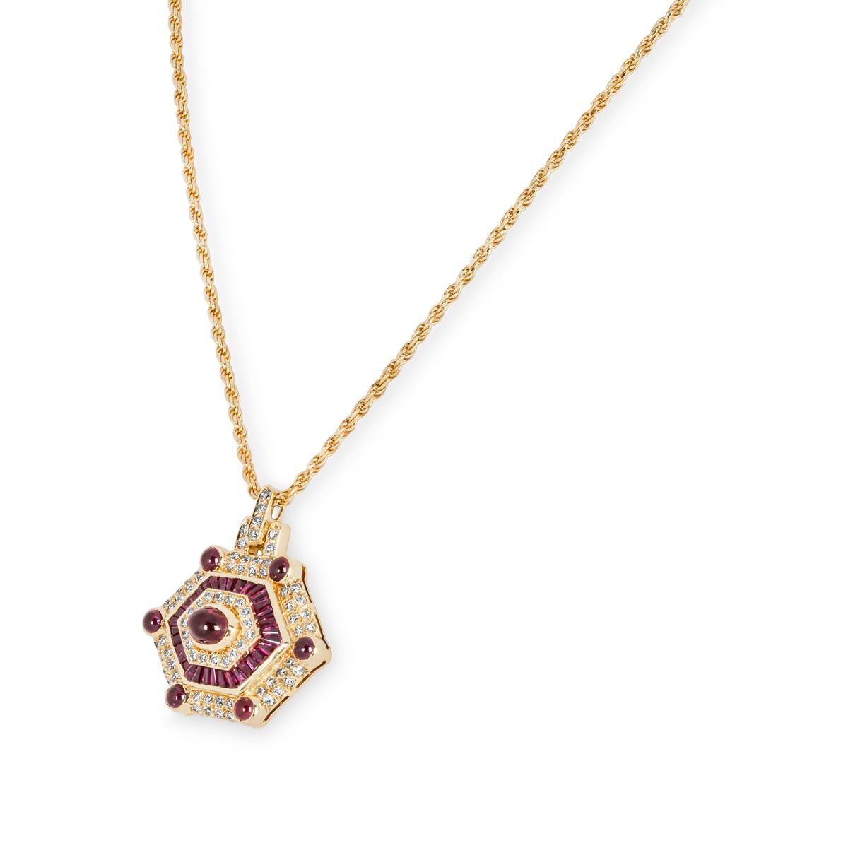 A beautiful 18k yellow gold ruby and diamond pendant. The necklace consists of a diamond set bail leading to a hexagon-shaped pendant. The pendant alternates between round brilliant cut diamonds, tapered baguette cut rubies and cabochon cut rubies.