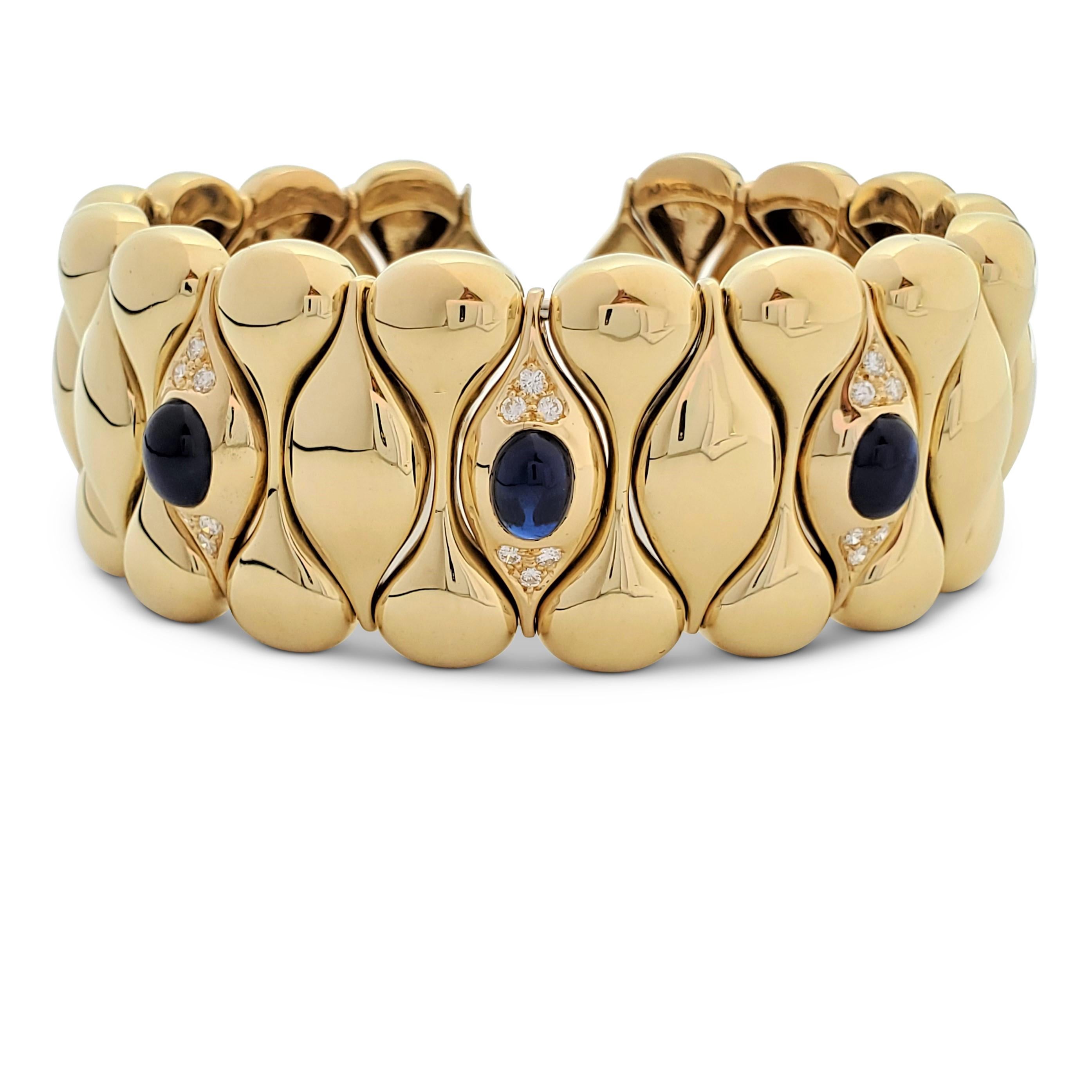 Wide cuff bangle crafted in 18 karat yellow gold comprised of alternating curved sections. Three of the center sections are accented with round brilliant cut diamonds (E-F color, VS) and cabochon blue sapphires. Marked 750. The bracelet is not