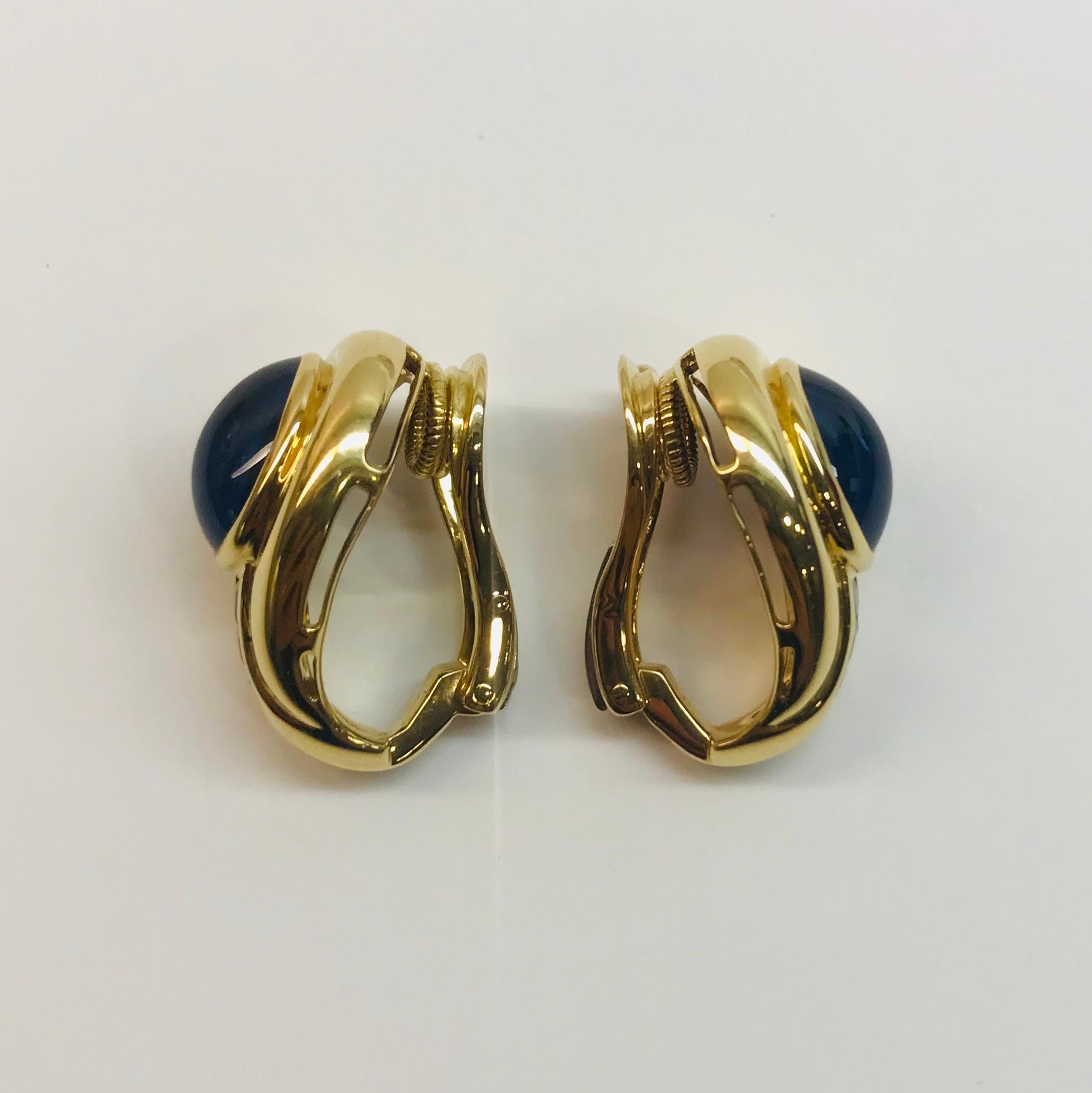 One pair 18K yellow gold and bezel-set cabochon-cut sapphire earrings with 6- accent baguette-cut, channel-set sapphires. The two cabochon-cut blue sapphires weigh approximately 7.84 cts and the six side blue sapphires total approximately 0.78 cts.