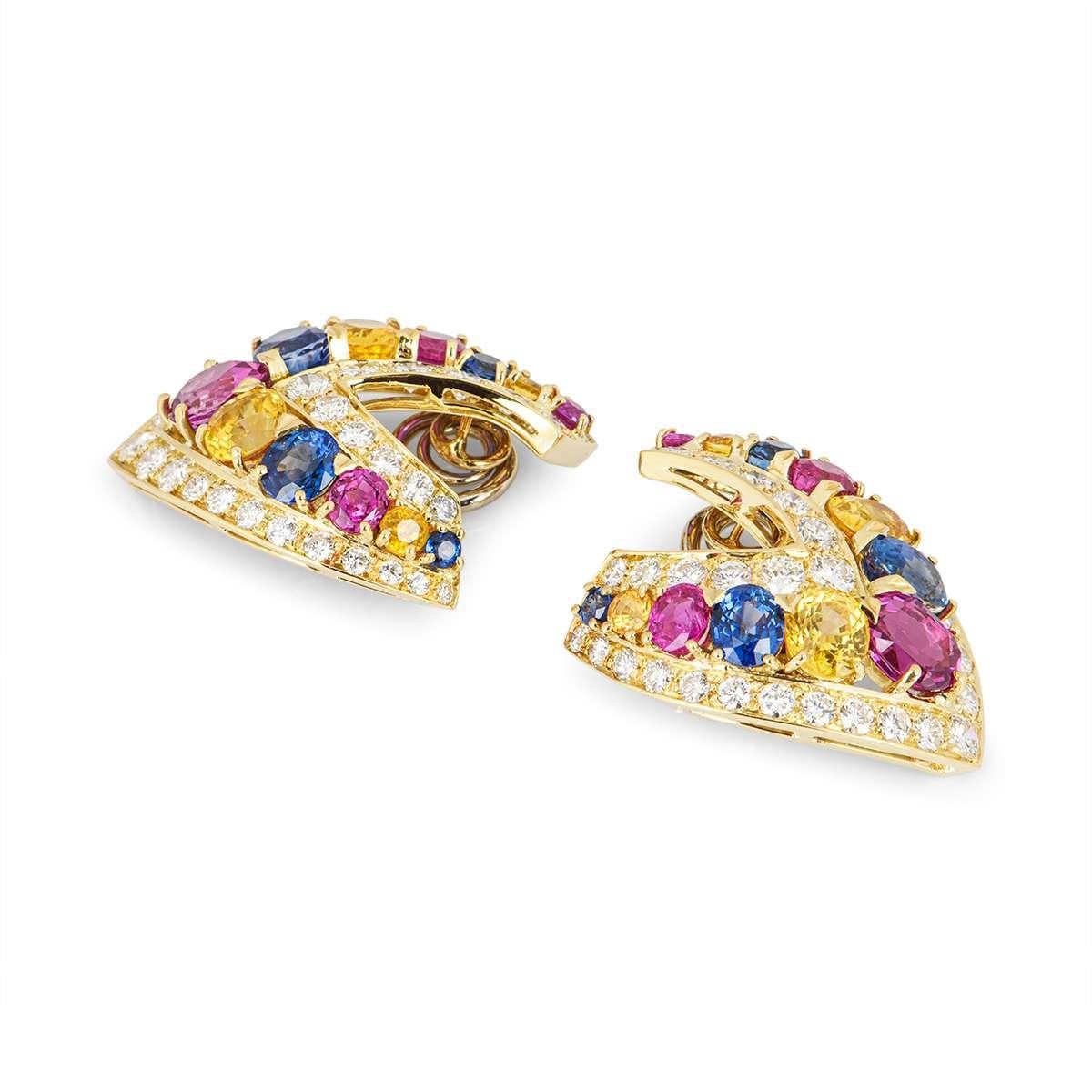An eye-catching pair of 18k yellow gold clip earrings. The earrings are V shaped and are set in the centre with an array of coloured sapphires, including pink, blue and yellow. There is a boarder of round brilliant cut diamonds set on either side of