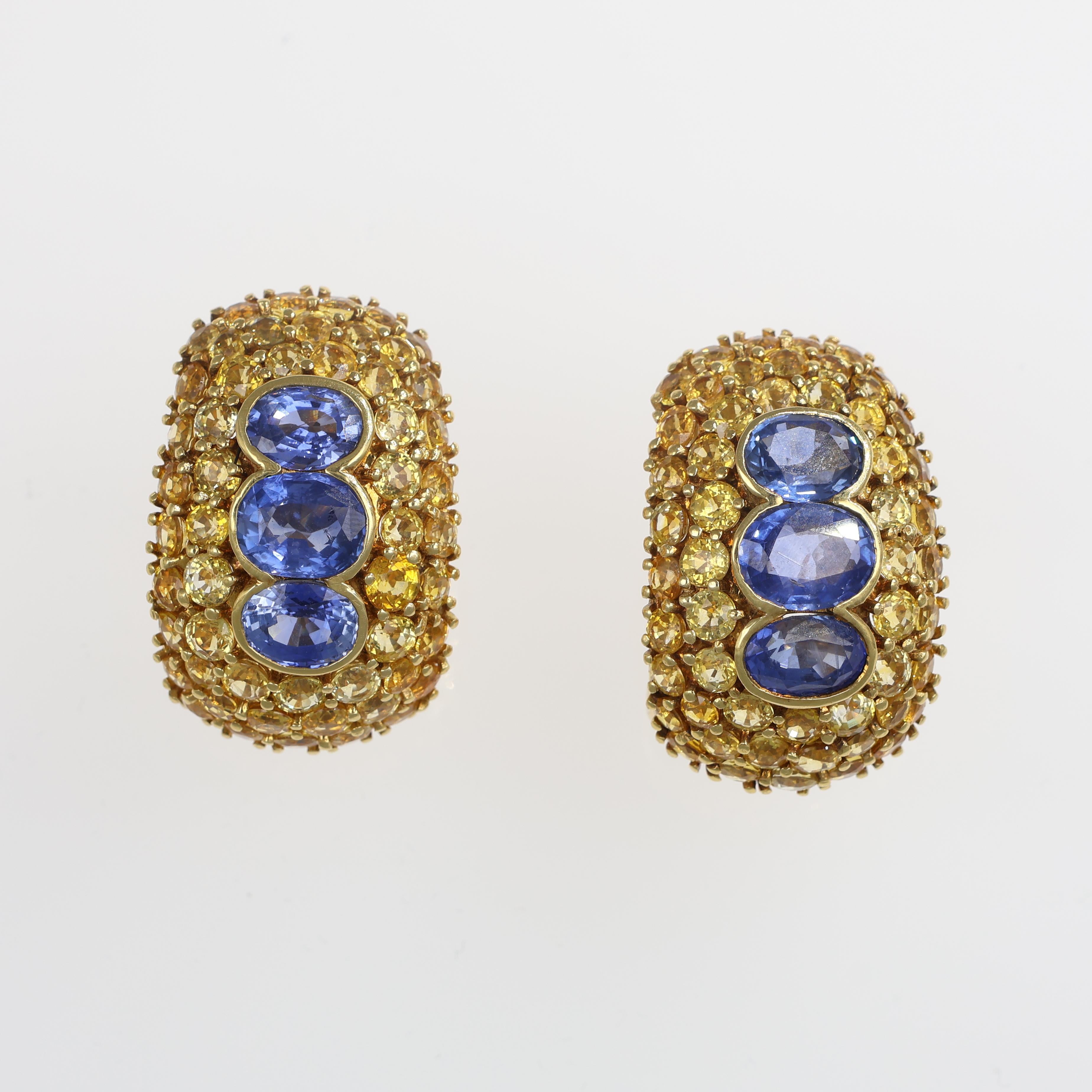 Bold and luxurious 18kt yellow gold stud earrings featuring a rich pavé of yellow sapphires, highlighted by a striking row of three vivid blue sapphires. A statement piece that combines warm and cool tones, designed for those who appreciate refined