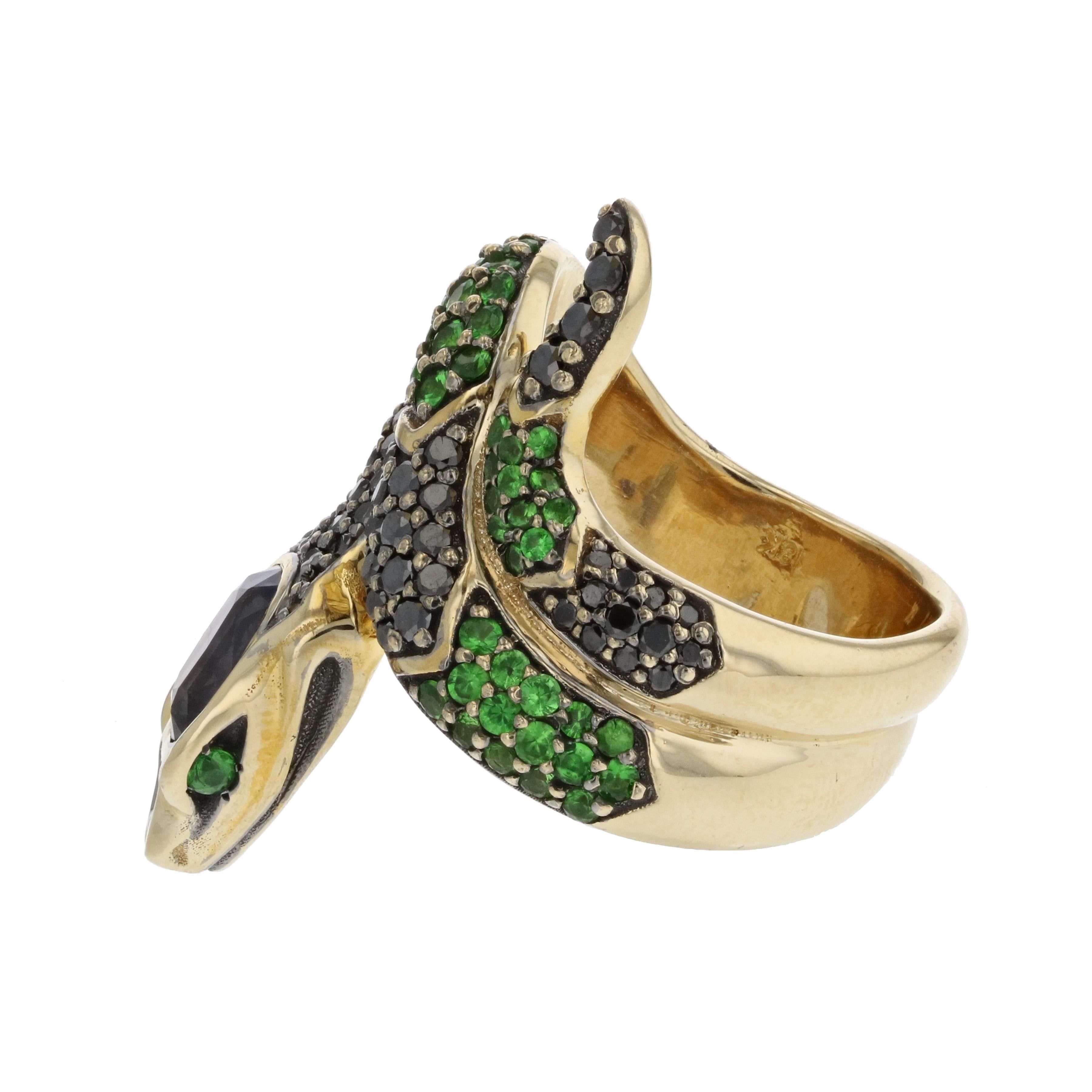 Snake ring composed of 18K yellow gold ring featuring a purple sapphire at the head, accented by tsavorite garnets and black diamonds.  The purple sapphire weighs 2.16 carats and is accompanied by a gemological report from Universal Gemological