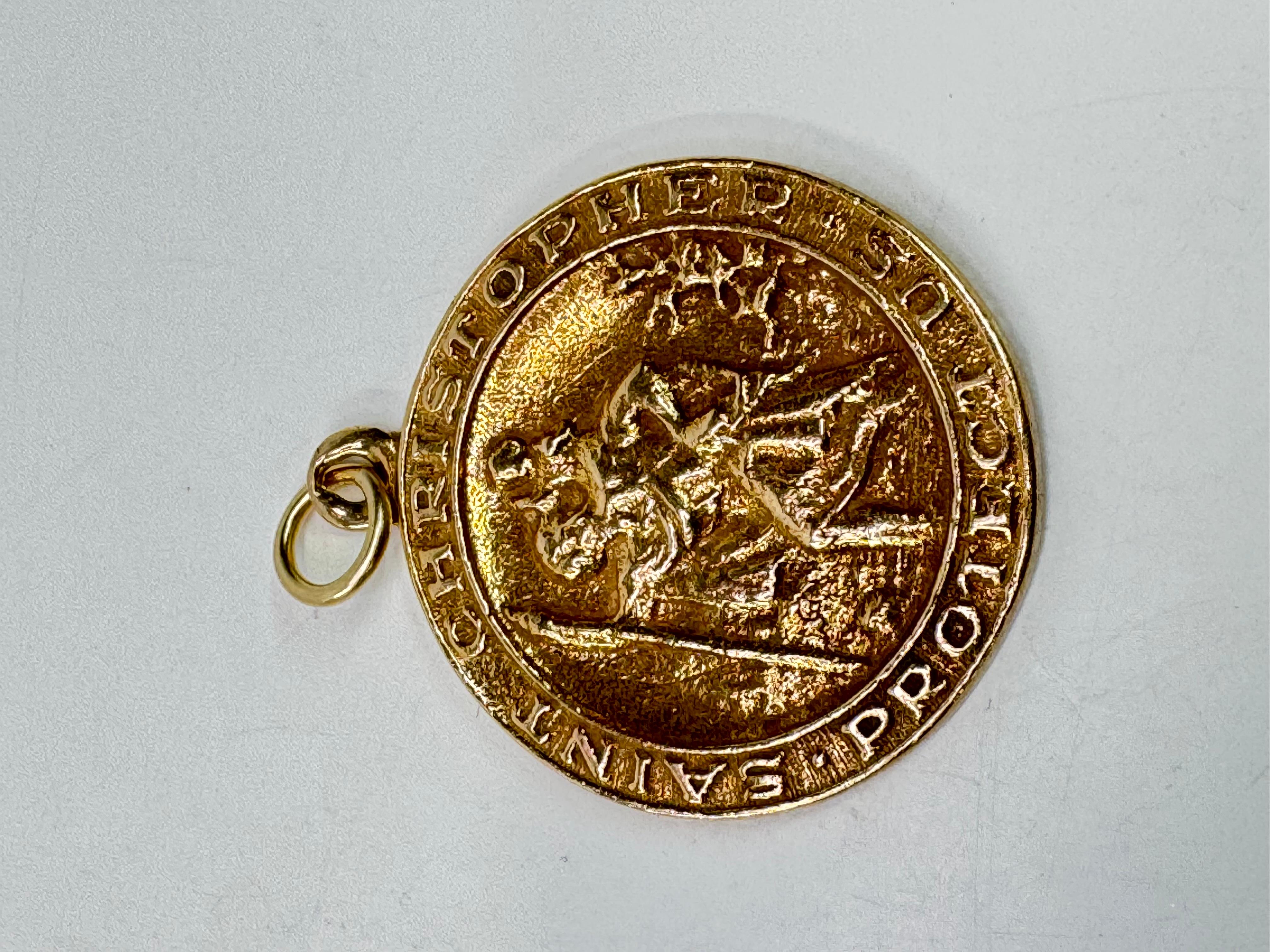 Questo pendente a forma di disco di San Cristoforo in oro 14 carati è un pezzo significativo e senza tempo. Con un diametro di 26,8 mm, il ciondolo presenta un'immagine dettagliata di San Christophe e l'iscrizione 