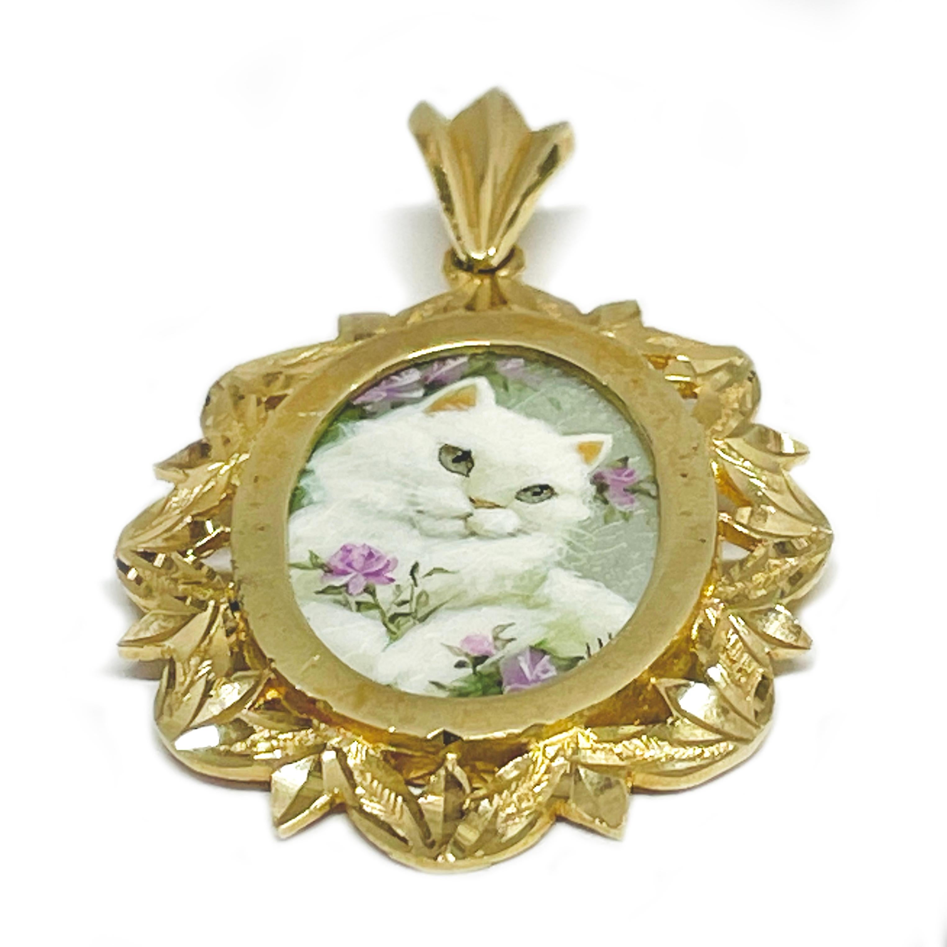 14 Karat Yellow Gold White Cat Hand Painted on a Mother of Pearl Pendant. The painting features a white cat with lavender flowers. The miniature painting is set in a 14 karat gold ornate oval frame with diamond-cut details. The painting is signed by