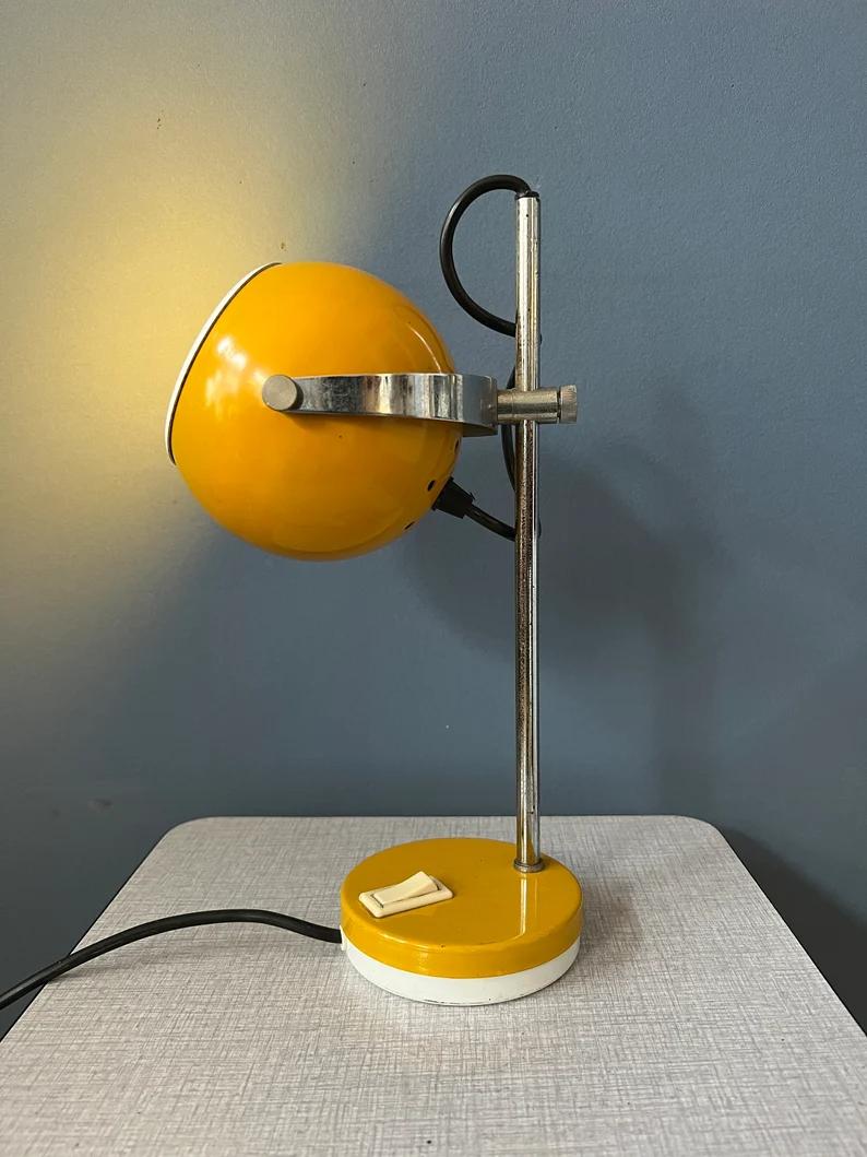 Lampe de table de l'ère spatiale en forme de globe oculaire jaune par la marque néerlandaise Herda. L'abat-jour en métal jaune peut être positionné de la manière souhaitée et se déplacer de haut en bas sur la base. La lampe nécessite une ampoule E27