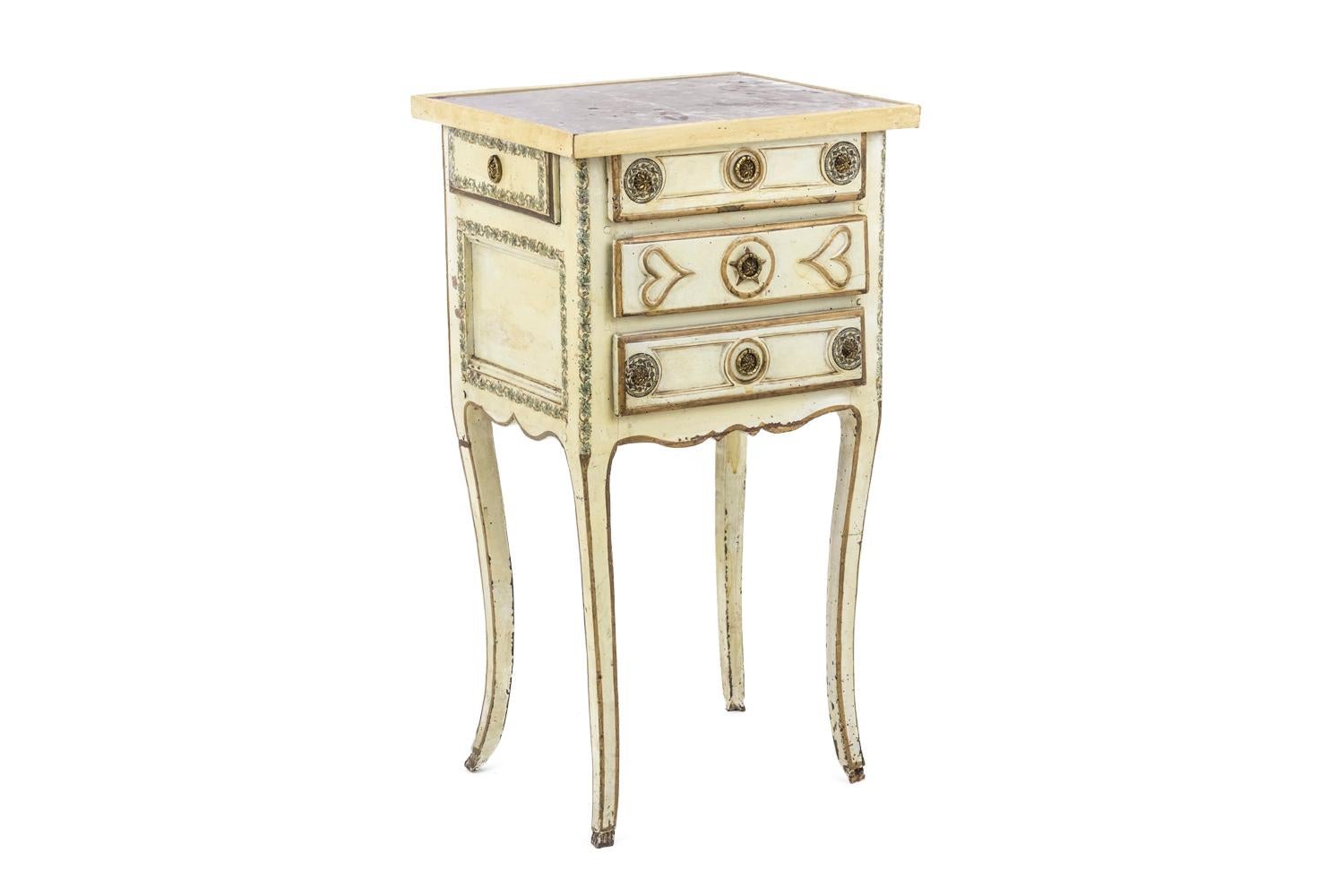 Bedside table in pale yellow lacquered wood standing on four cabriole legs.
Opening by three drawers on the front and a drawer on the right side. Carved decor of hearts and circles on drawers completed by a grey-brown painted decor of small flowers