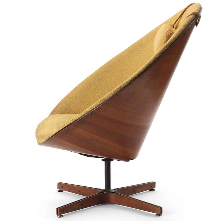 A swiveling and tilting lounge chair, the seating element formed of walnut plywood with seamless integral upholstery resting on a four-pronged wood-clad base. Retaining the original yellow linen and headrest.