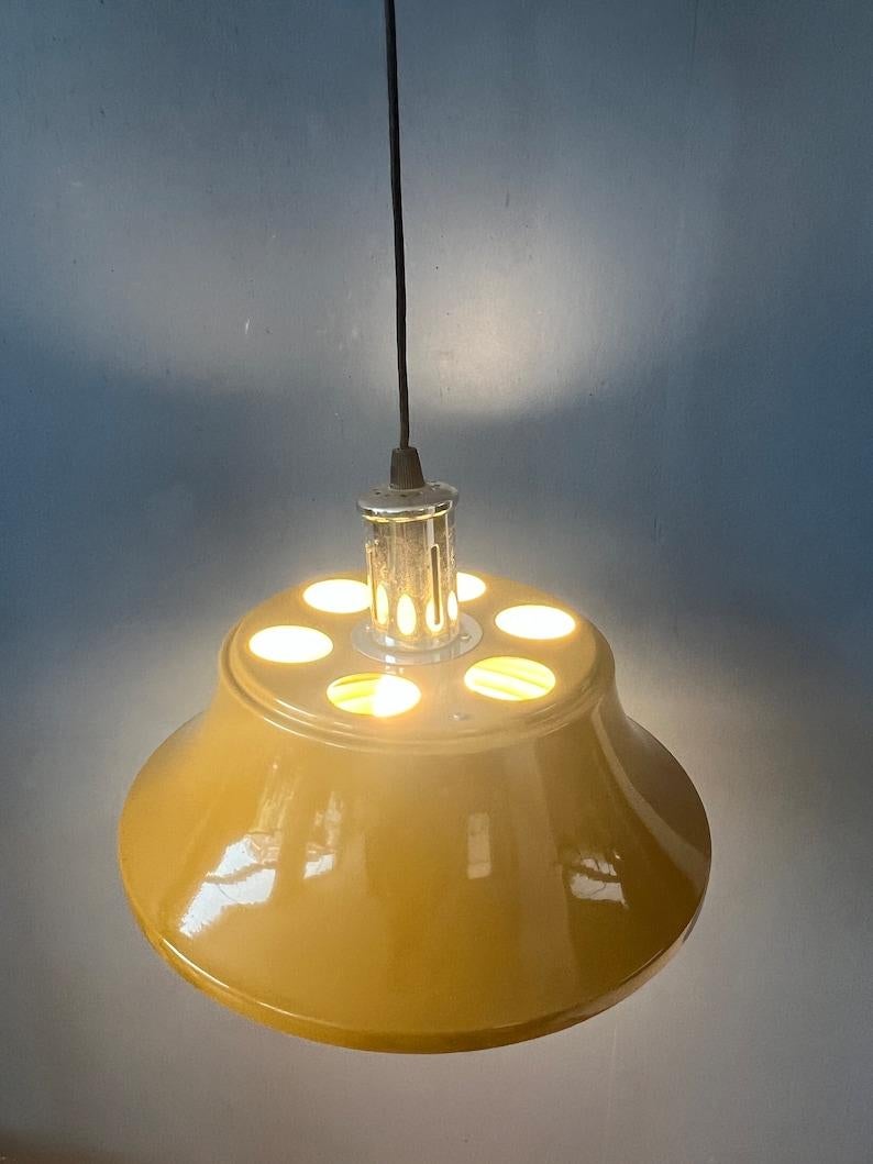 Lampada a sospensione gialla di metà secolo realizzata in metallo. La lampada è laccata di giallo lucido. Sotto la lampada c'è un roster in plastica che distribuisce bene la luce. La lampada richiede una lampadina E27/26.

Informazioni