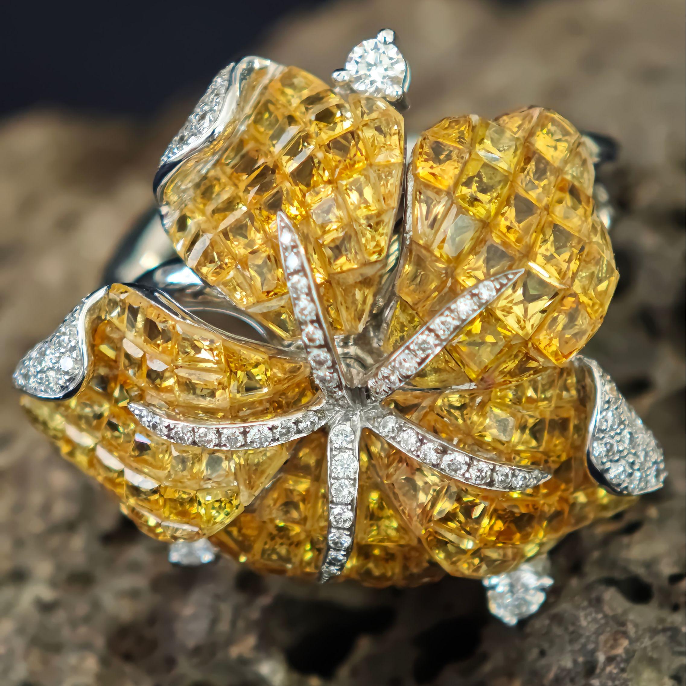Faites une déclaration audacieuse avec cette magnifique bague à fleurs, fabriquée de manière experte dans 10 grammes d'or blanc luxueux 18K. Dotée d'une monture invisible unique, la bague met en valeur 7,18ct de saphirs jaunes naturels vibrants