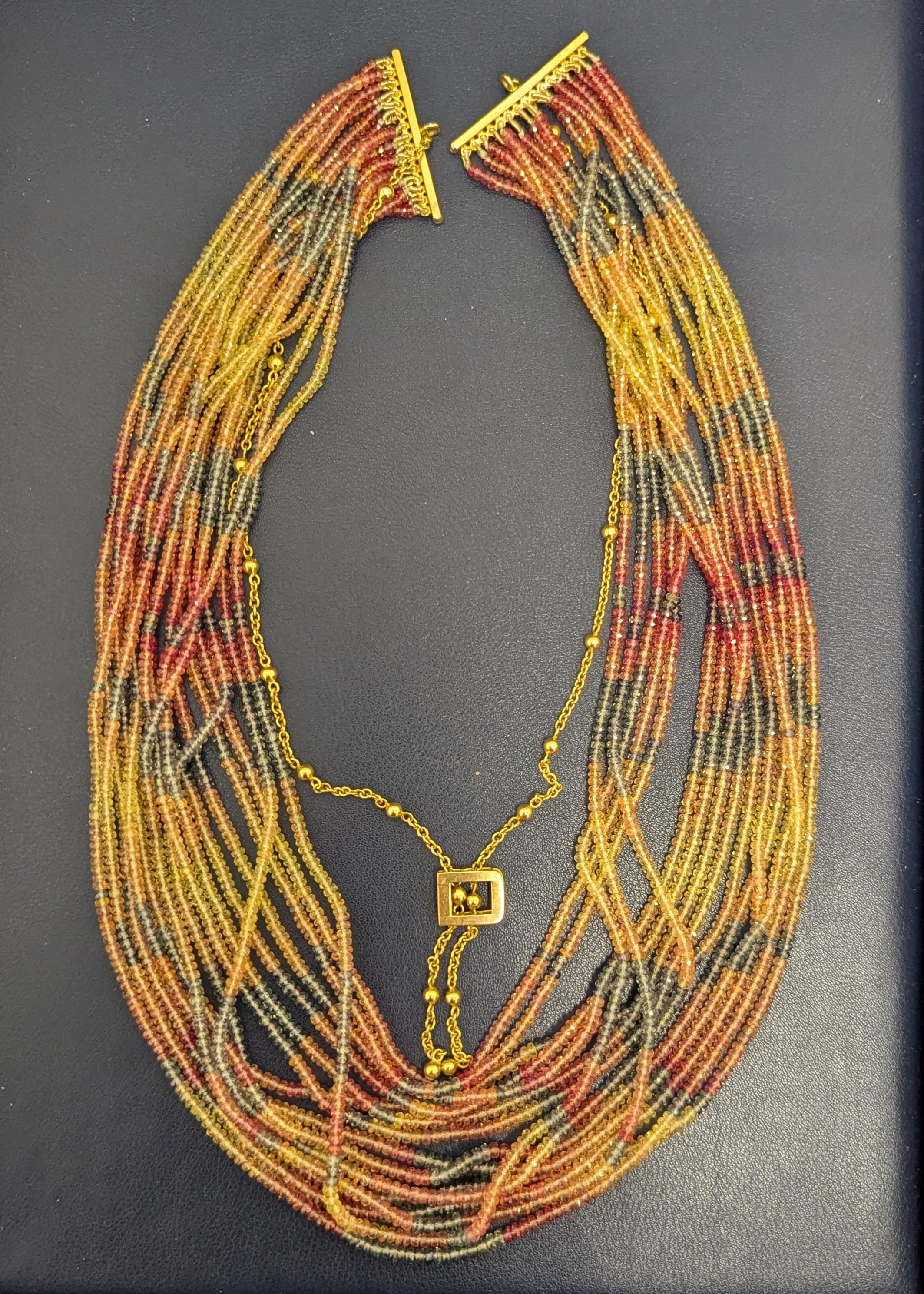 This playful, 15-strand multicolored necklace features various shades of yellow, orange, pink and slightly bluish green lively beads, woven onto a 14K yellow gold rods and a chain, which features an adjustable closure. 