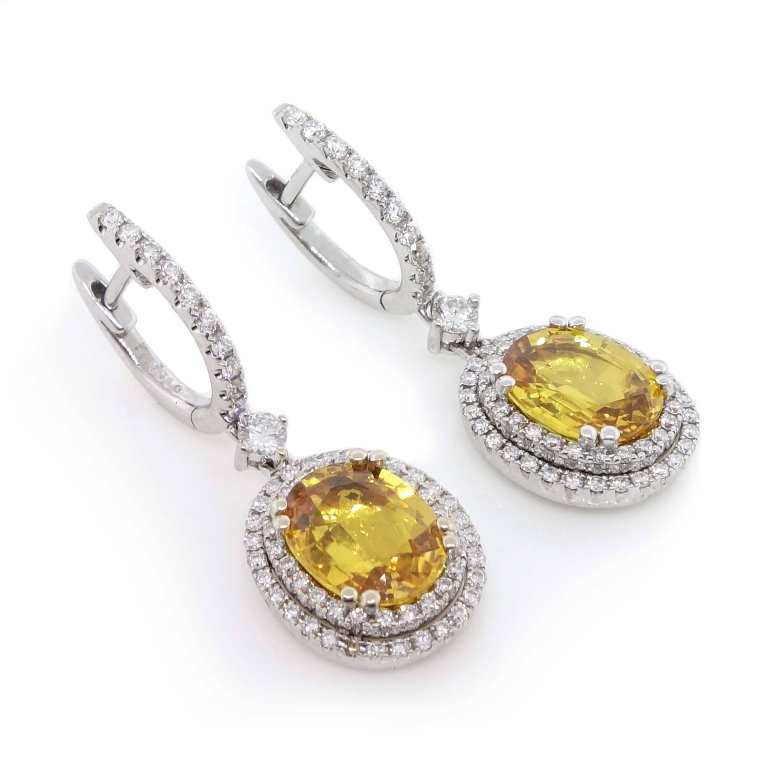 Dangle earrings containing 2 fine yellow oval Sapphires of about 5.81 carats measuring approximately 9.86×7.78×3.80mm and 9.74×7.80×3.76mm. The sapphires are surrounded by 128 round brilliant cut Diamonds of about 0.90 carats. It also contains 2