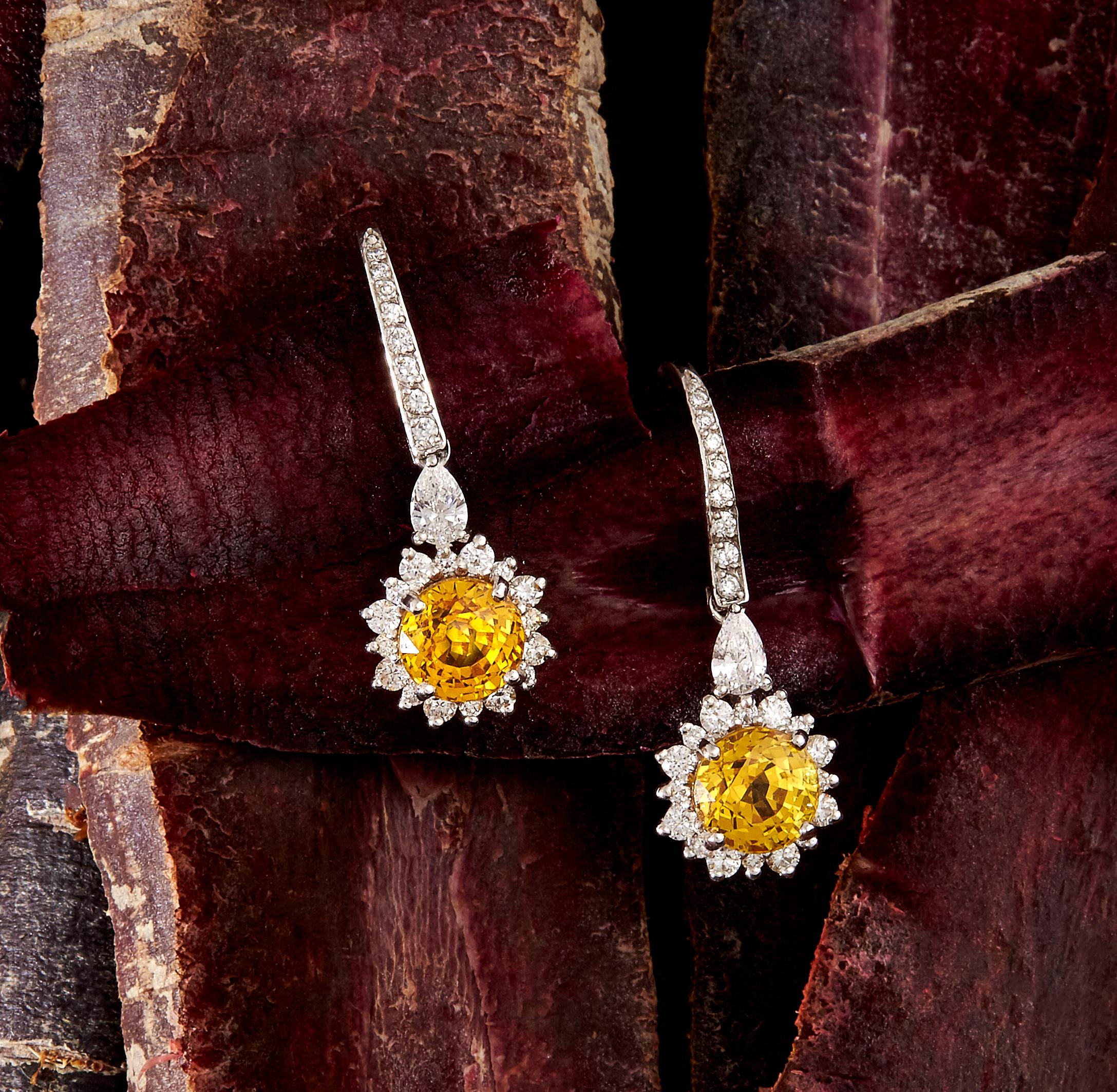 Matthew Ely 18 carat white gold drop earrings set with 2 round cut yellow sapphires amounting to 2.96ct. Surrounding the sapphires are two pear shaped diamonds of F color and VS-SI clarity that total 0.20ct, and 48 round diamonds of F color and VS