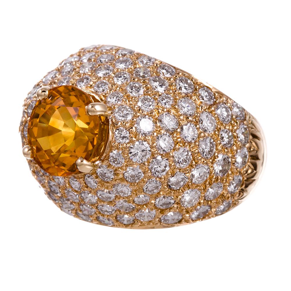 A classic dome ring with diamonds cascading down the shoulders of the architecture, the ring is rendered in 18 karat yellow gold and topped with a 4 carat intense yellow-orange sapphire. This ring offers a lovely balance of sophistication and