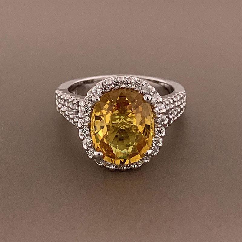 A gemset ring featuring a nearly 5 carat (4.98ct) yellow sapphire. The stone is cut in an oval shape and has a clean vivid yellow color. It is accented by 0.68 carats of round brilliant cut diamonds which halo the sapphire and run along the two