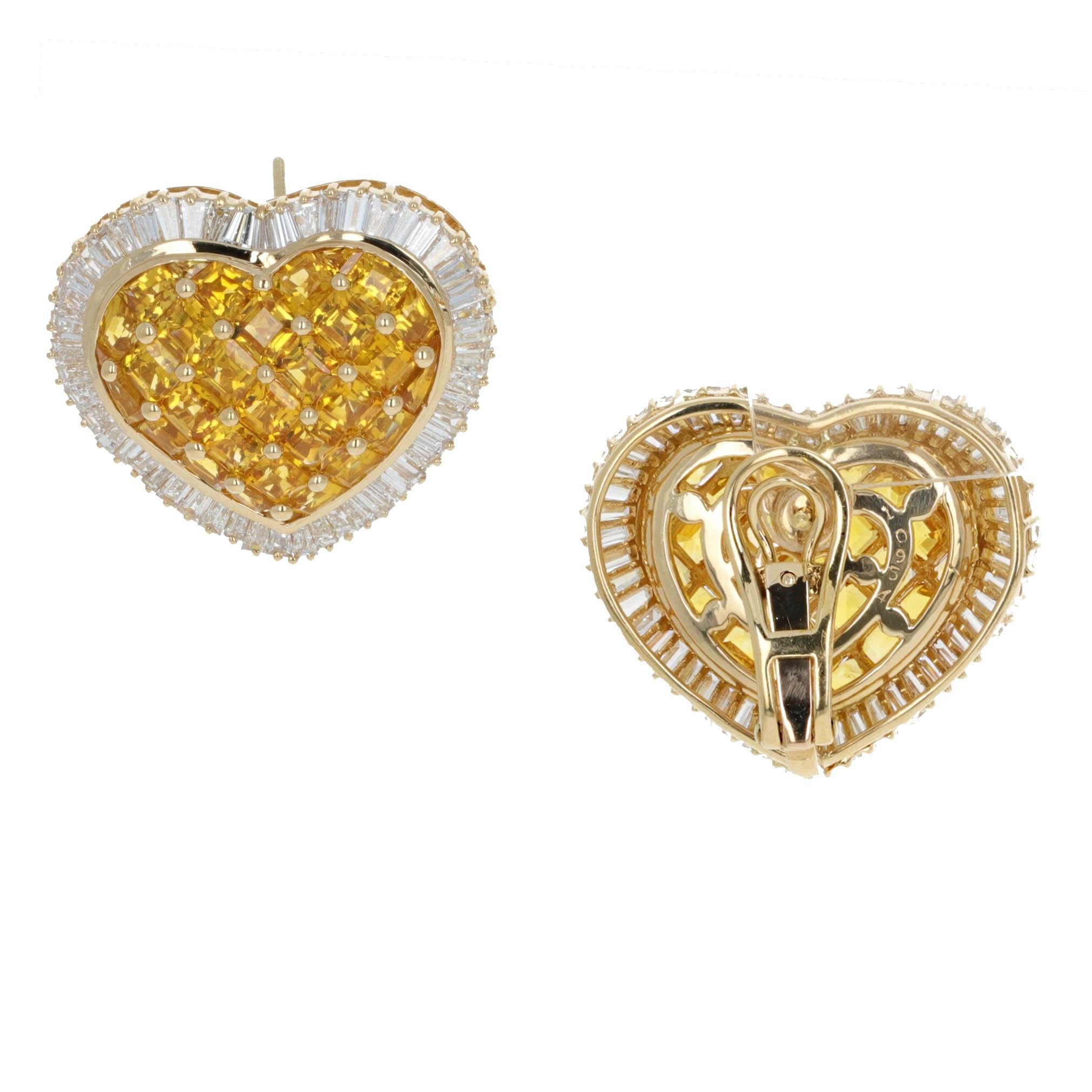 These 18k yellow gold heart-shaped earrings feature 19 carats total weight of vibrant yellow sapphire carree-cut gemstones, surrounded by 10 carats total weight of tapered baguette diamonds in a shimmering halo design. Measuring 1 inch in height and