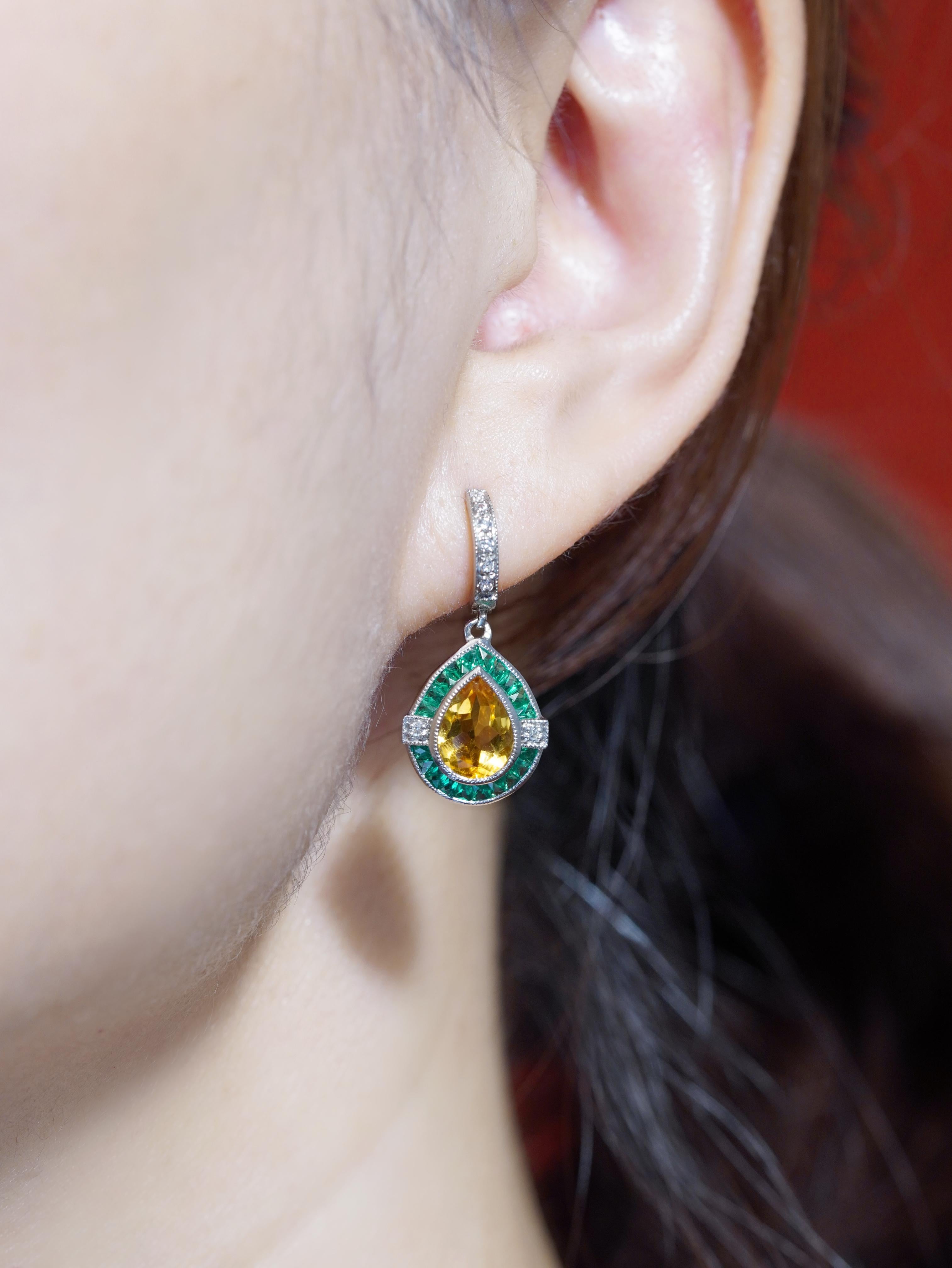 Un saphir jaune radieux en forme de poire au centre, magnifiquement encadré par des émeraudes vibrantes qui créent un contraste saisissant. Des diamants étincelants sont délicatement sertis autour du design, ajoutant une touche de brillance et