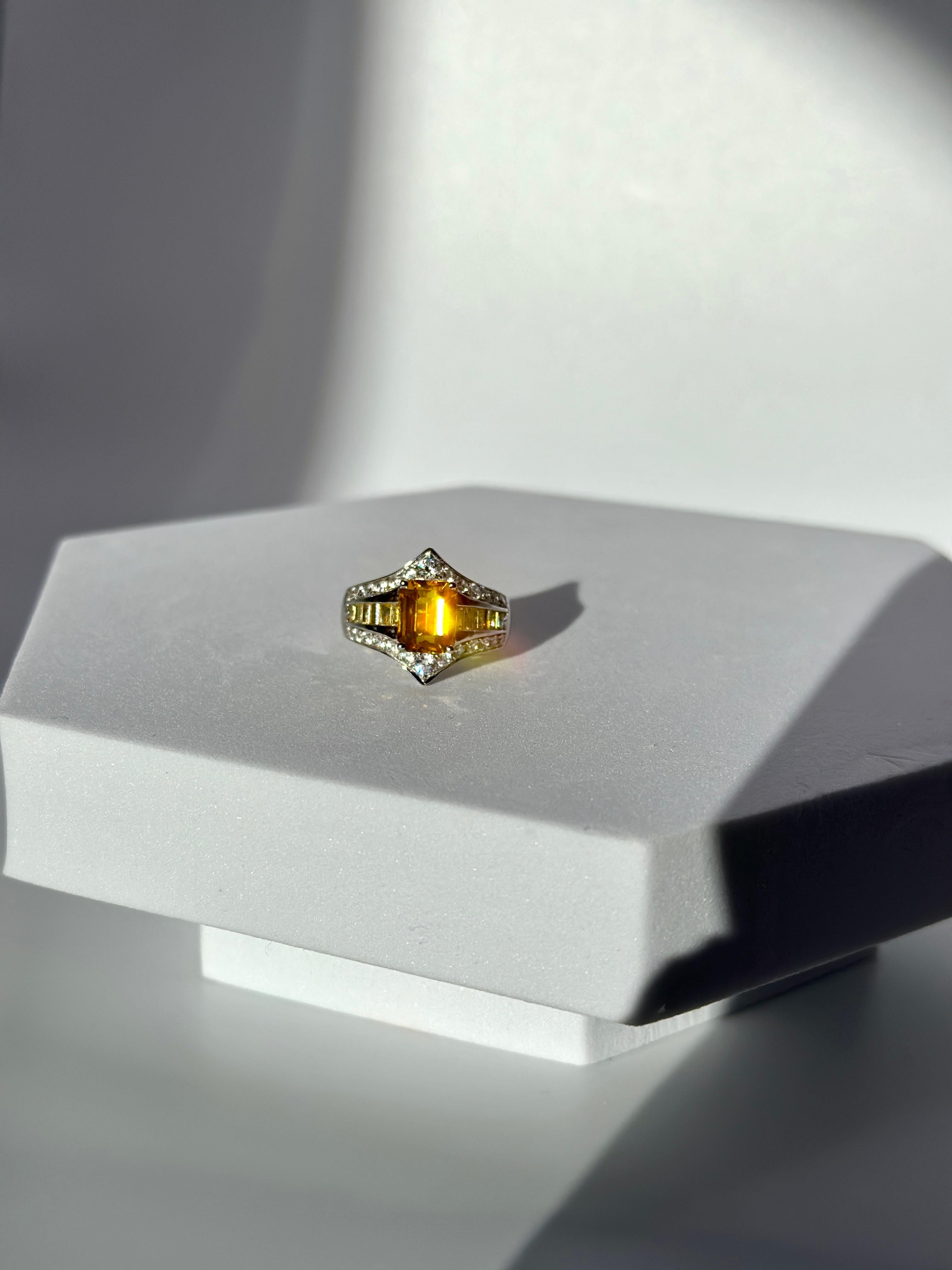 2ct emerald cut natural yellow sapphire on a 9k gold setting, a shield shape, meant to protect and may wealth and riches be drawn your way.
 the colorless stones are cubic zirconia, yellow ones are natural yellow sapphires. 