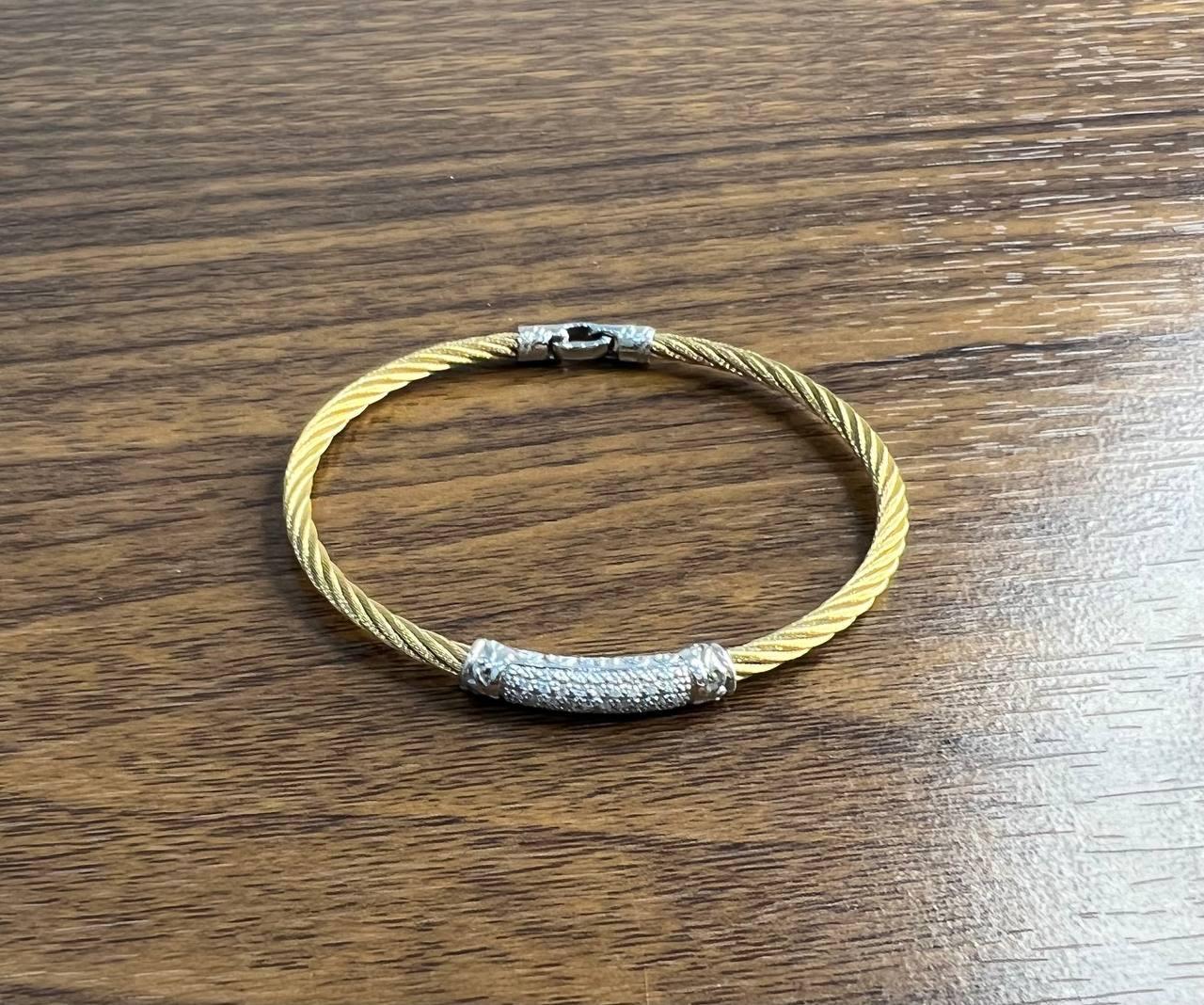 Crafted with a twisted gold-tone steel cable design, featuring a central bar encrusted with shimmering pave diamonds . Accented with 18K White Gold details. 0.30 ctw Diamonds. G/VS Quality