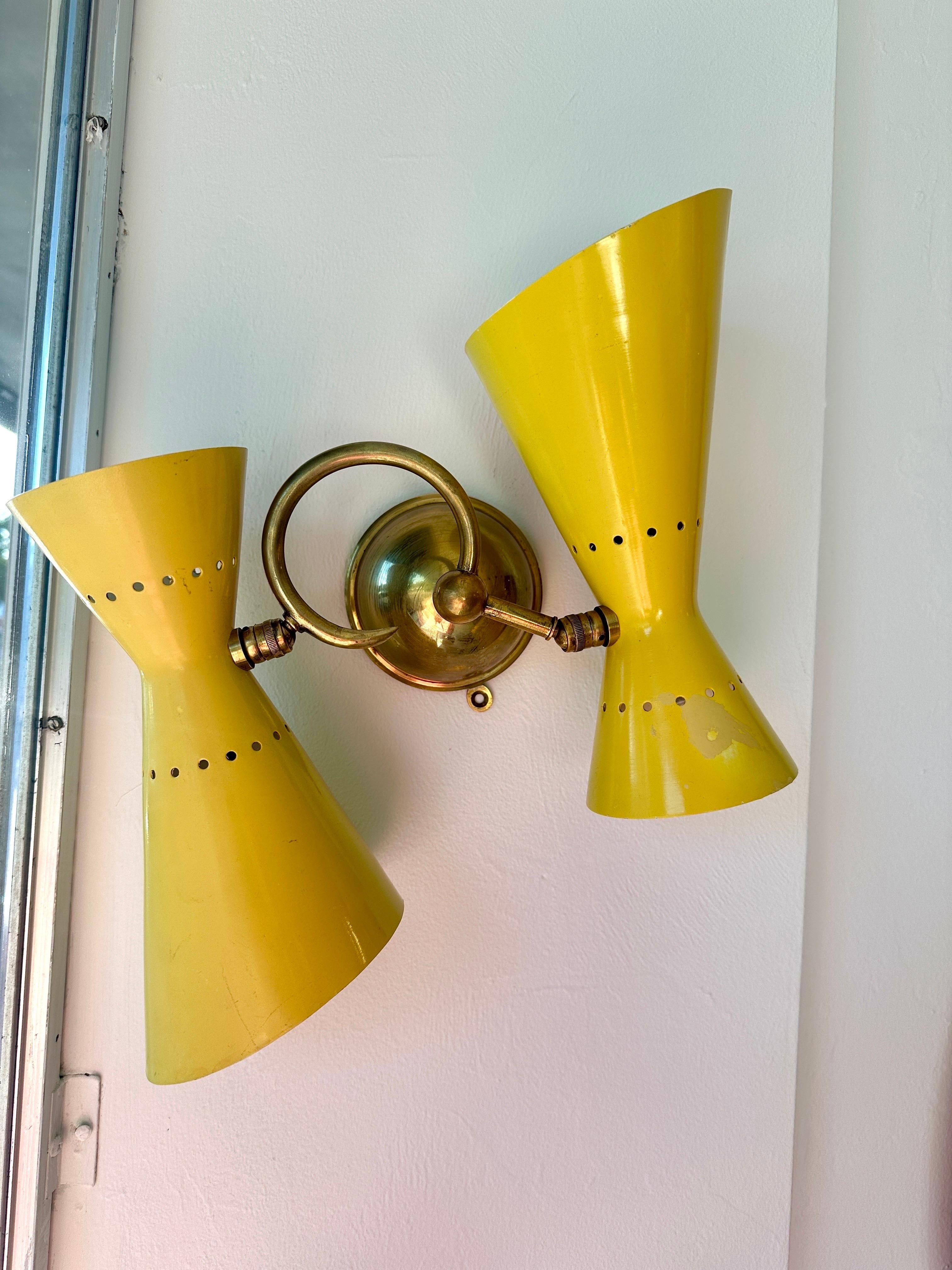We offer here very FUN Stilnovo vintafe perforated cone wall lights in original vivid yellow. Brass wall mount and curved arms hold these yellow metal cones that are each double lights (up and down) - total of 4 bulbs/ lights per sconce. We have a