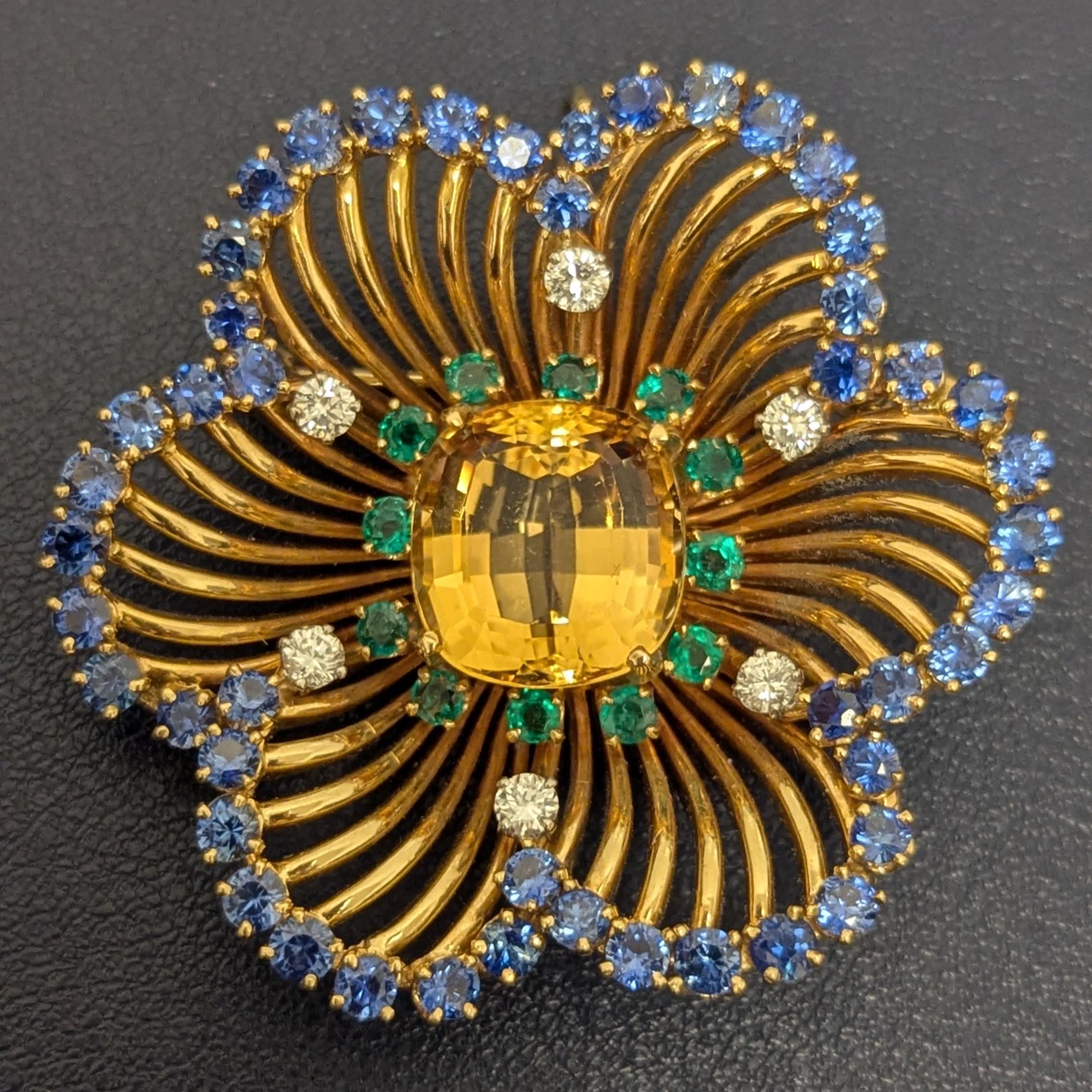 This intricately designed piece can be worn as both a pendant and a brooch. The 14K Yellow Gold is set with one centering fancy-cut topaz and enhanced with round emeralds, sapphires, and full-cut diamonds. 
