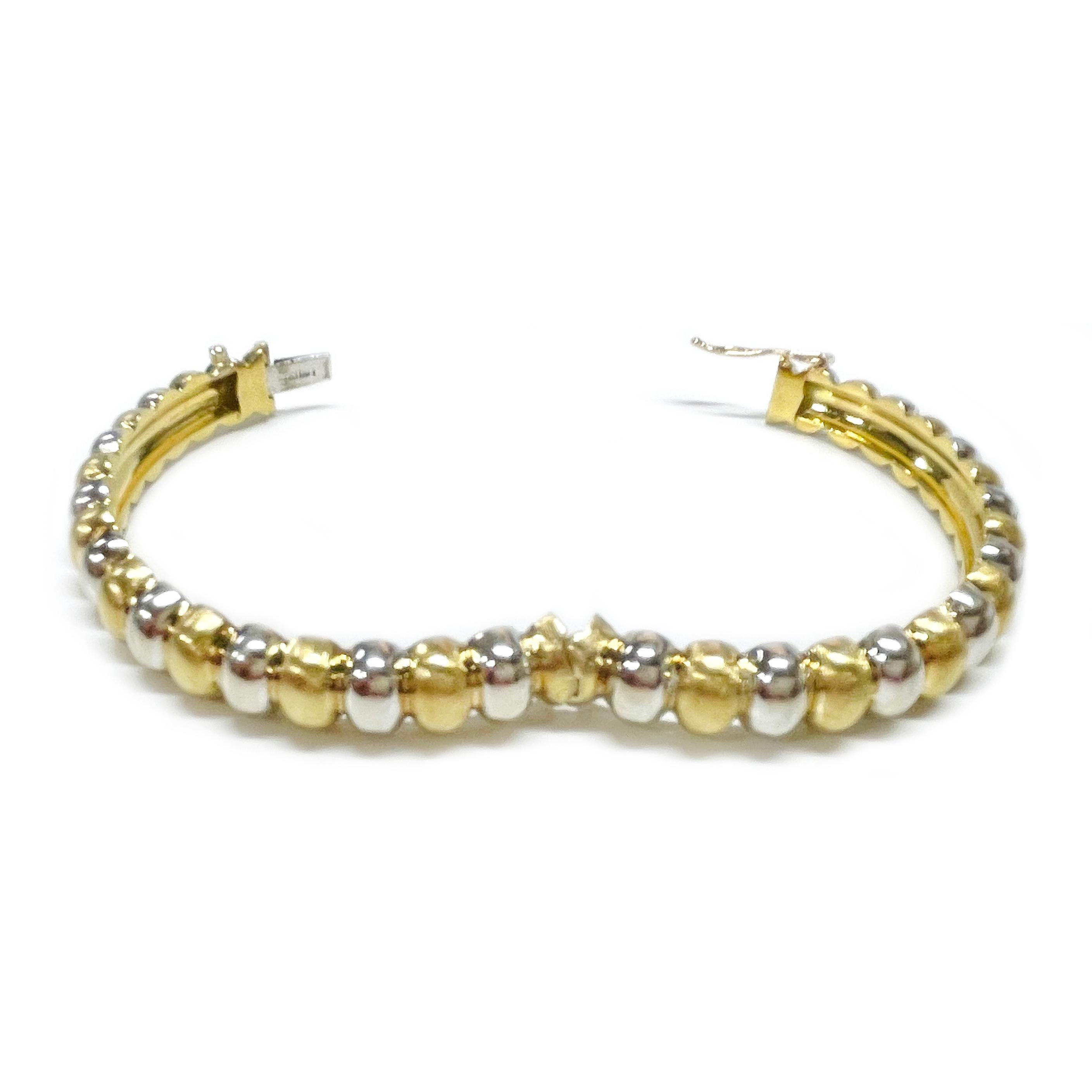 18 Karat Yellow & White Gold Hinged Bangle Bracelet. The bangle bracelet features alternating yellow and white ovals. The white ovals have a smooth shiny finish and the yellow gold ovals have a textured finish. The bracelet measures 68.19 x 63.90 x