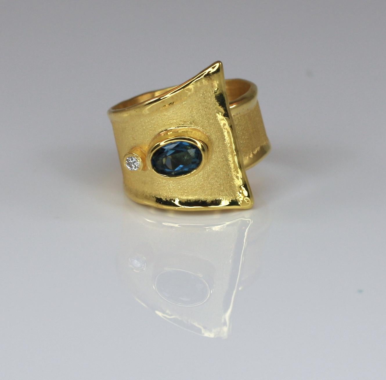 Yianni Creations artisan ring crafted in Greece from 18 Karat Yellow Gold. Shiny liquid edges contrast with the brushed texture of the surface. This geometrical ring features a 1.60 Carat oval cut London Blue Topaz accompanied by a 0.03 Carat