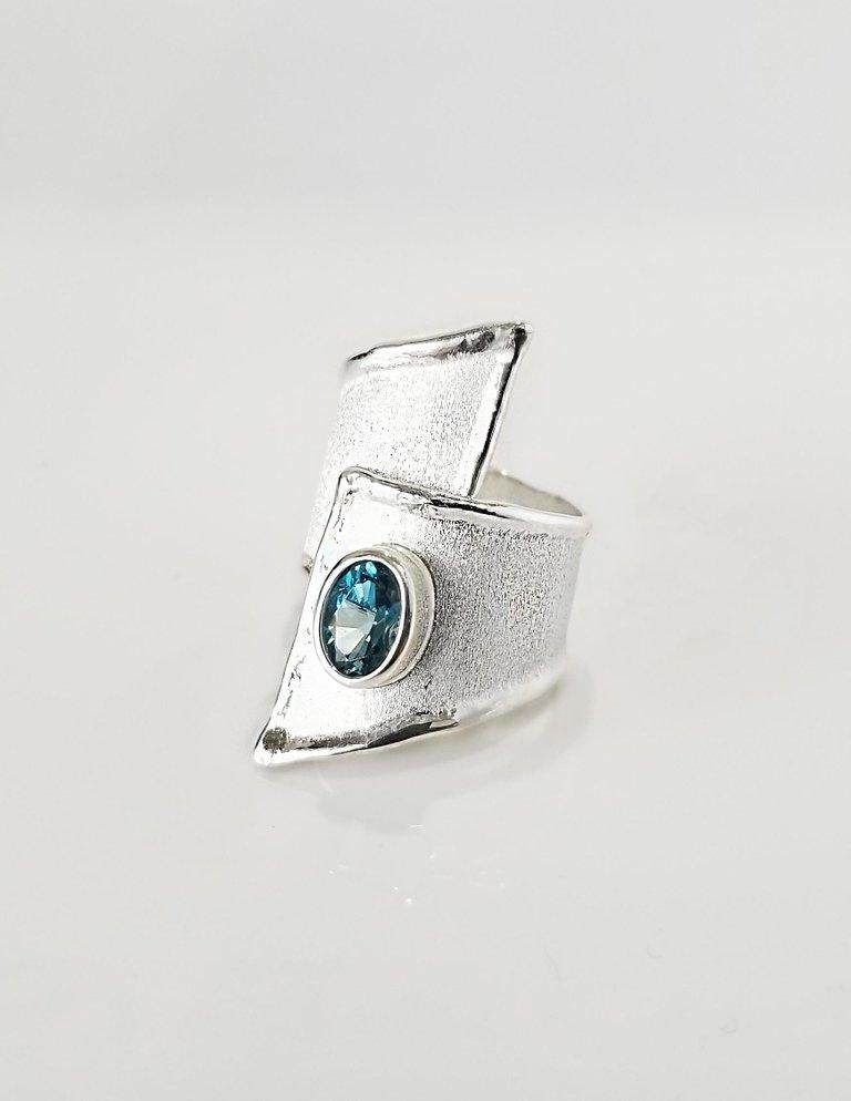Yianni Creations presents Ammos Collection handmade artisan ring from fine silver 950 purity plated with palladium. This wide asymmetrical ring features 1.60 Carat London Blue Topaz on mat brushed texture and shiny nature-inspired liquid edges. The