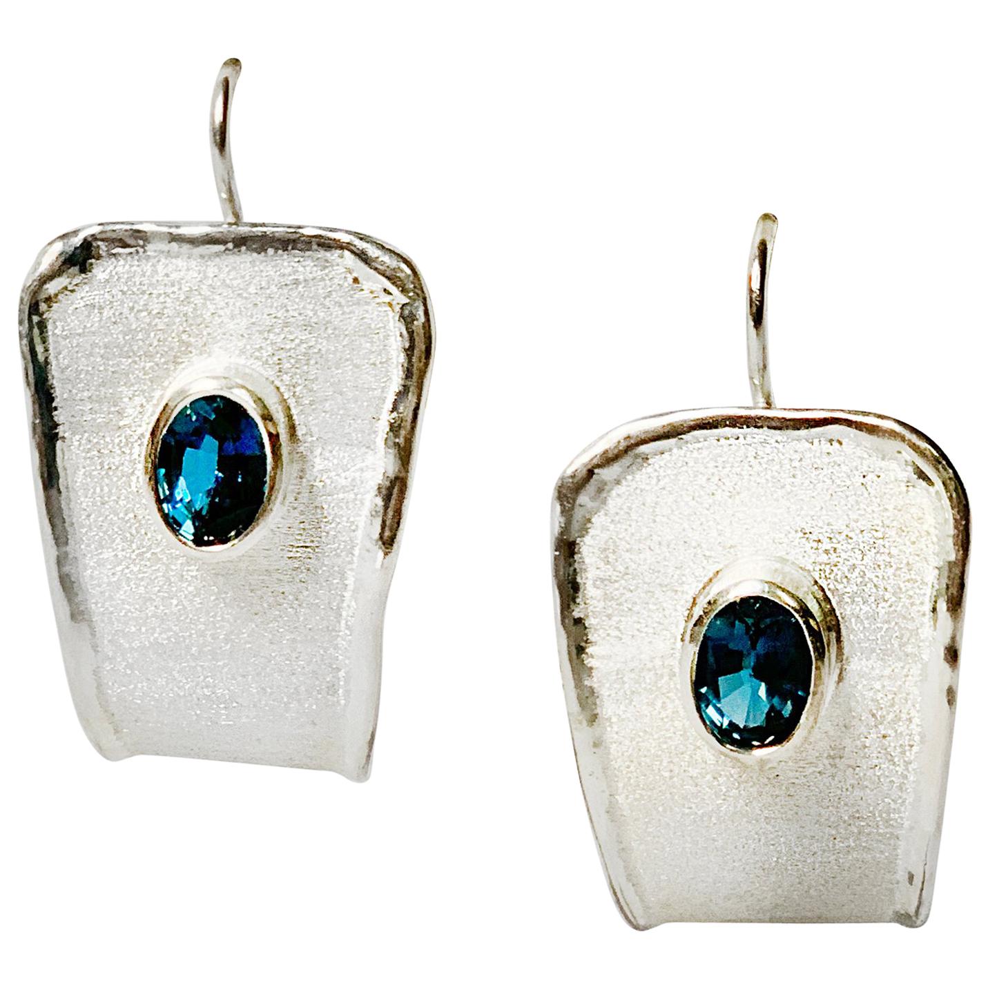 Yianni Creations Ammos Collection 100% Handmade Artisan Dangle Earrings from Fine Silver. Each earring features 1.20 Carat Oval Cut London Blue Topaz complemented by unique techniques of craftsmanship - brushed texture and nature-inspired liquid