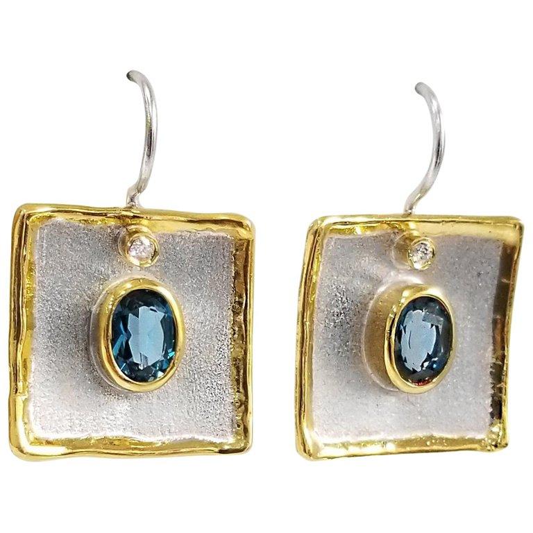 Yianni Creations Midas Collection 100% Handmade Artisan Earrings from Fine Silver with a layover of 24 Karat Yellow Gold feature each 1.60 Carat Oval Cut London Blue Topaz accompanied by 0.03 Brilliant Cut Diamond complimented by unique techniques