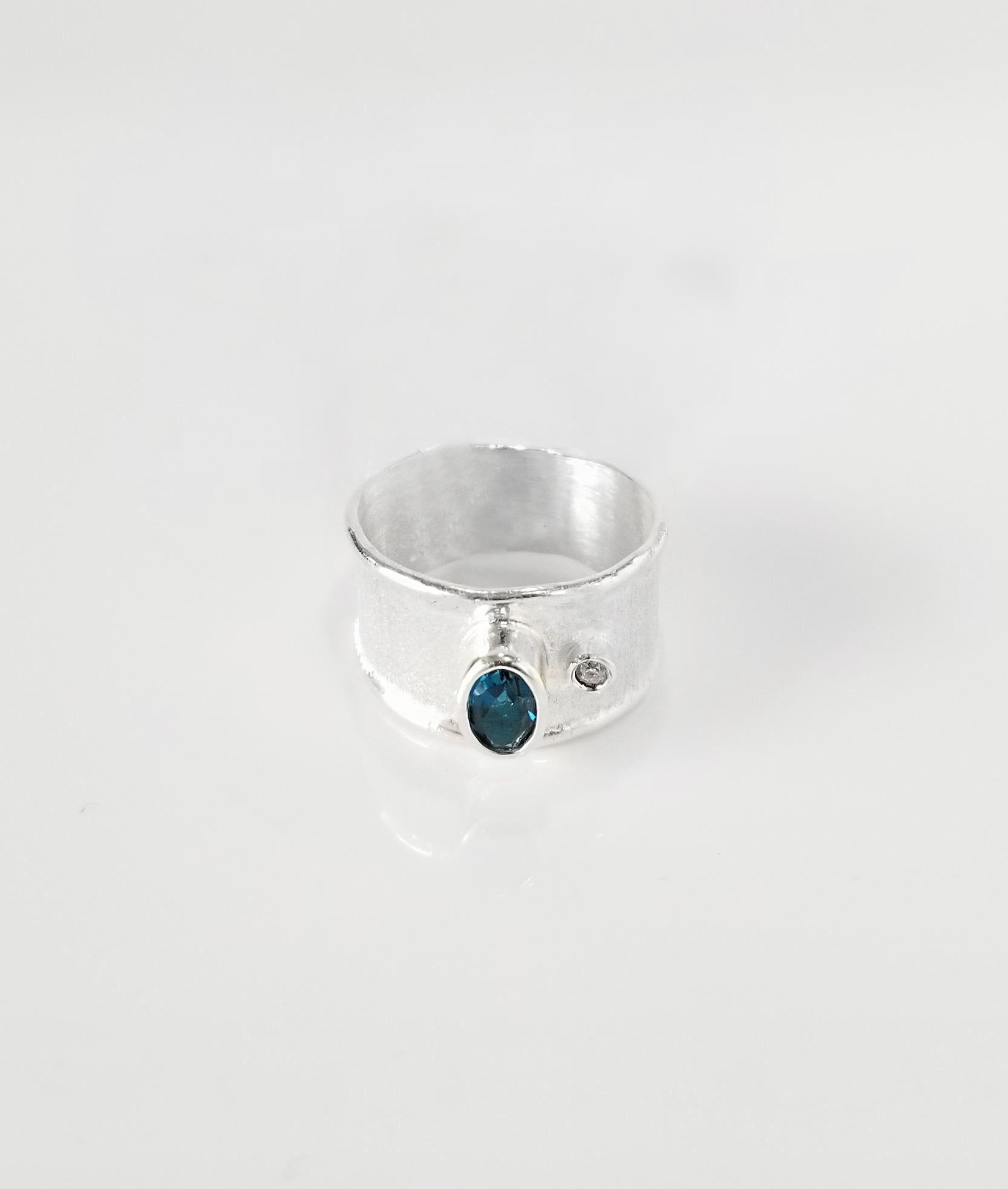La bague en argent fin de la collection Ammos de Yianni Creations est 100% artisanale et présente une topaze bleue de Londres de 0,40 carat accompagnée d'un diamant blanc taille brillant de 0,03 carat, le tout agrémenté de techniques artisanales