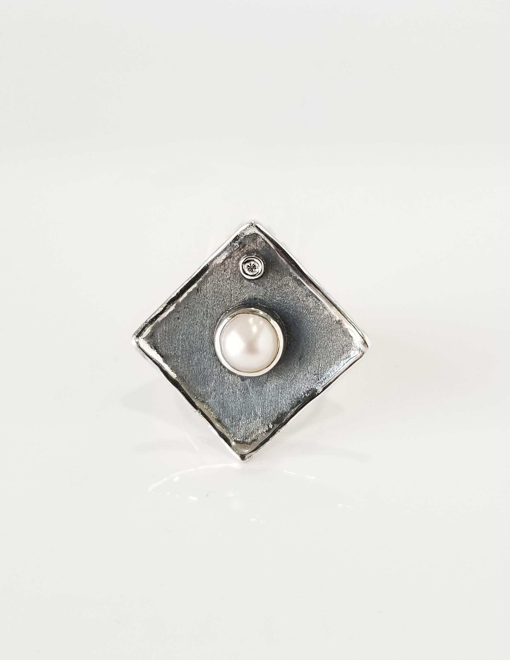 Yianni Creations Hephestos Collection 100% handgefertigter handwerklicher Ring aus Feinsilber. Ring mit 7 - 7,5 mm Süßwasserperle und 0,03 Karat Diamant im Brillantschliff auf einzigartigem, oxidiertem Rhodiumhintergrund. Die Edelsteine werden durch