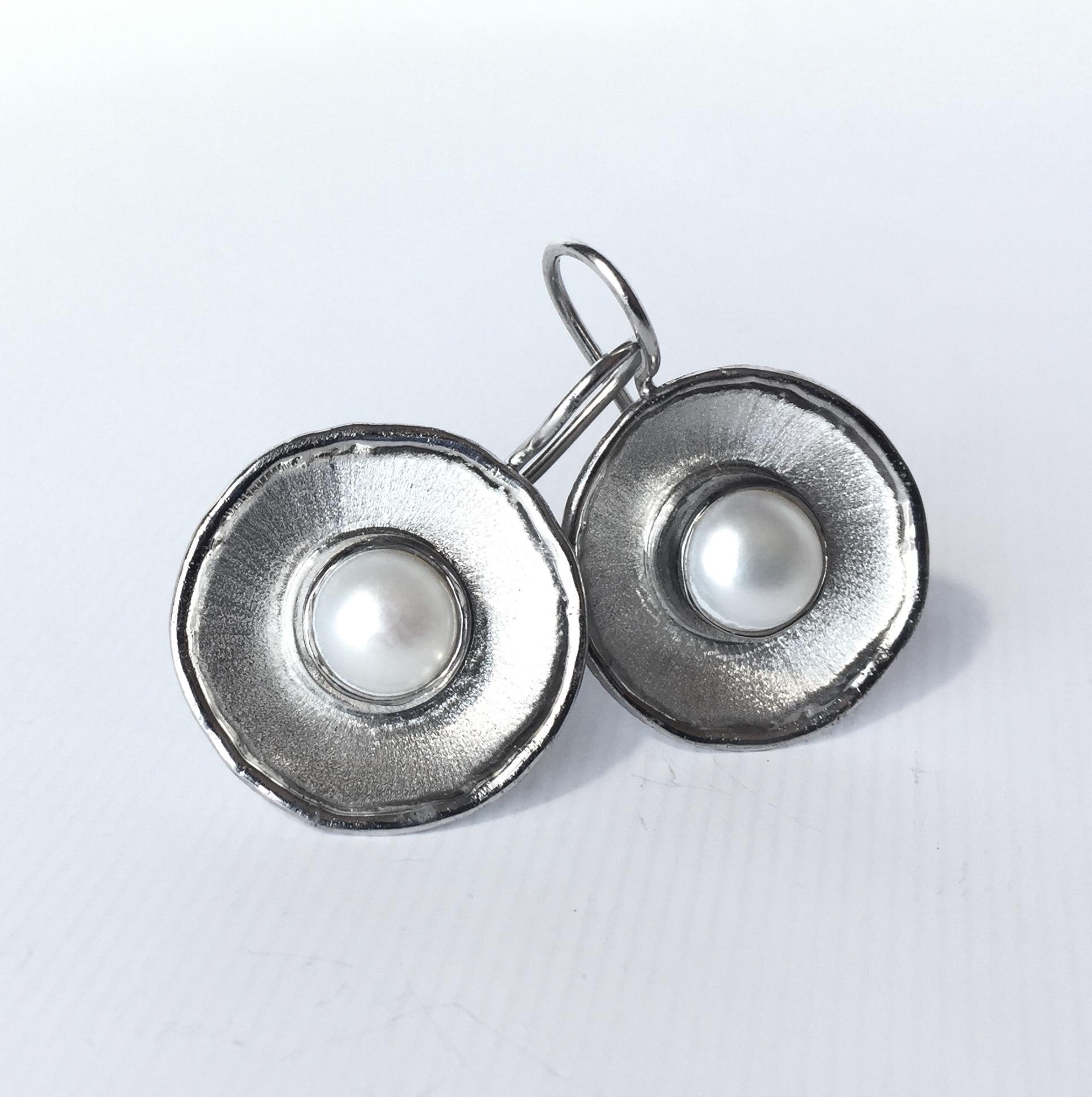 From Yianni Creations Ammos Collection, these are handmade artisan earrings from a fine silver plated with palladium to resist against elements. Each earring feature a 7mm round freshwater pearl. These round dangle earrings combine contrast of mat
