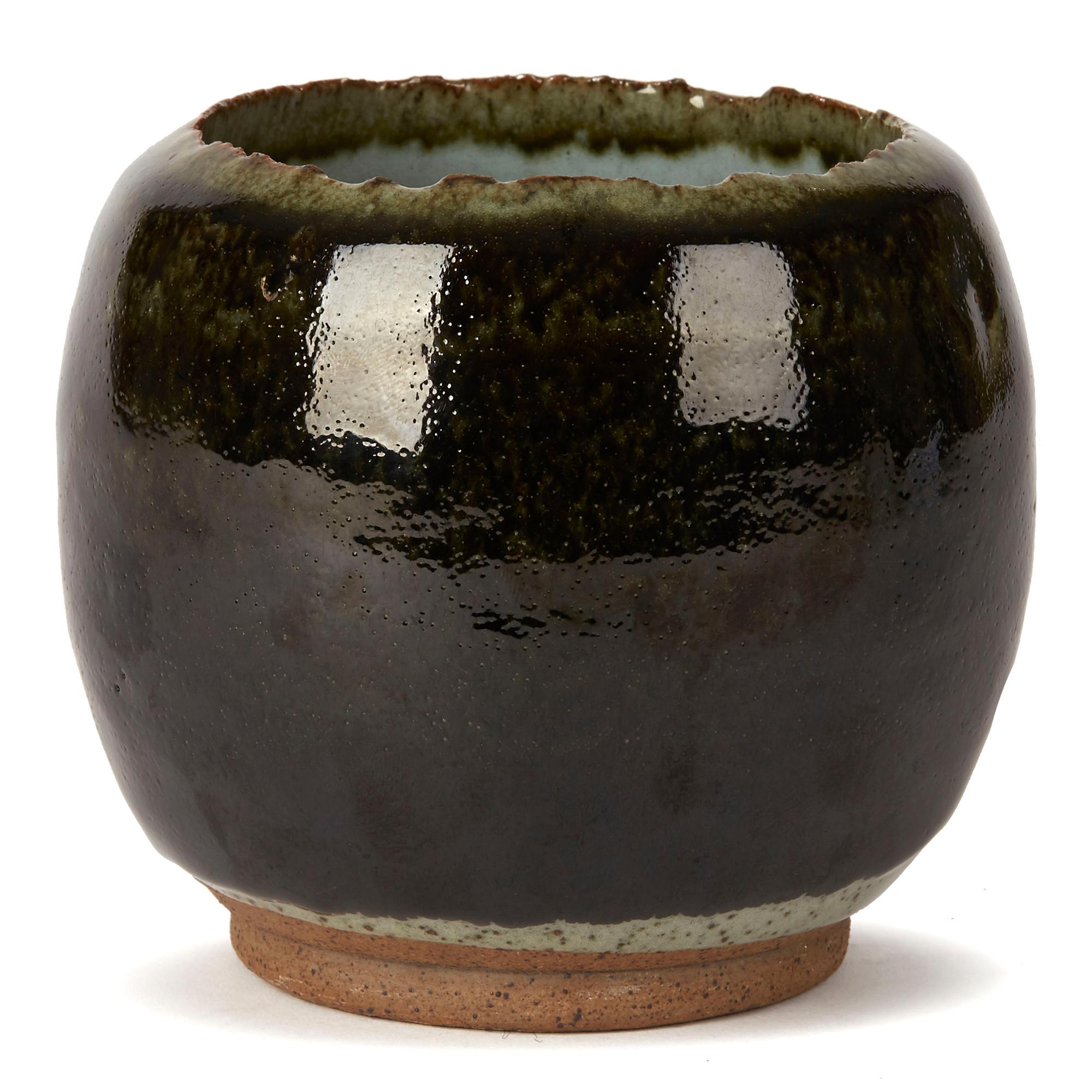 A hand thrown Studio Pottery stoneware vase decorated in green glazes by Ying Yeung Li (B.1951). The heavily potted vase stands on a narrow rounded unglazed foot and has a roughly cut top rim with the body applied on grey stone glazes with the outer