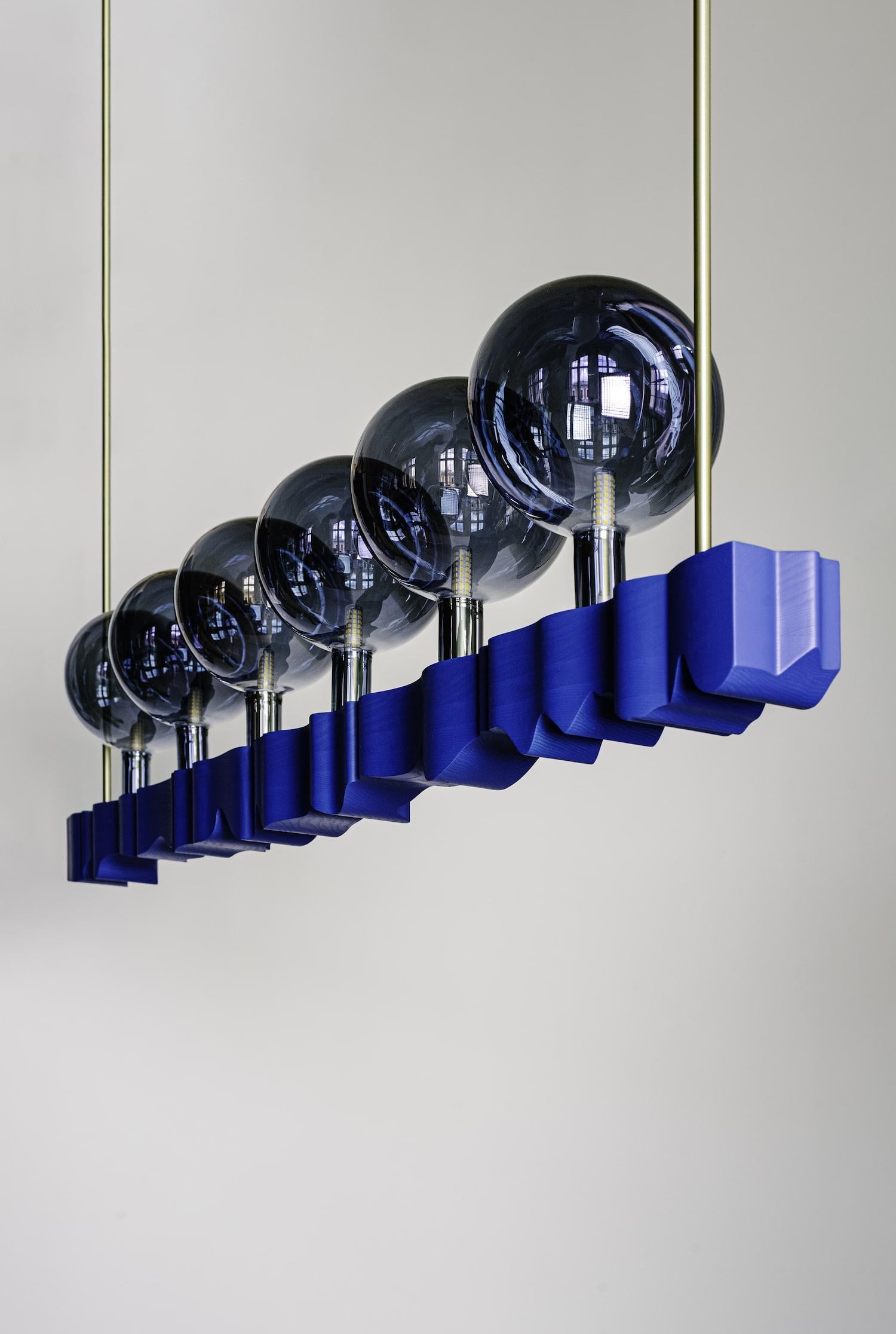 The monumental luminaire made of lacquered solid as wood in combination with brass construction and metal coated glass spheres. The aesthetics of the chandelier is an expressive interpretation and reference to the work of Czech architect Jan Kotěra
