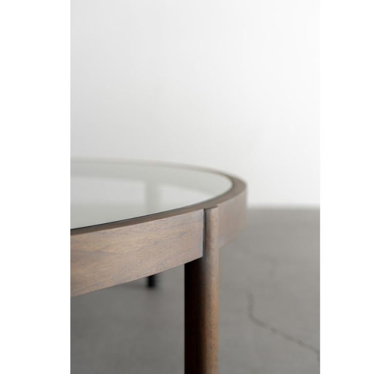 La table basse Ynez est fabriquée à la main à Los Angeles, en Californie. Le cadre en noyer est plié et moulé à la main. Le plateau en verre est soutenu par des pieds en noyer massif. Chaque pied présente un détail à la base, inspiré des rangées de