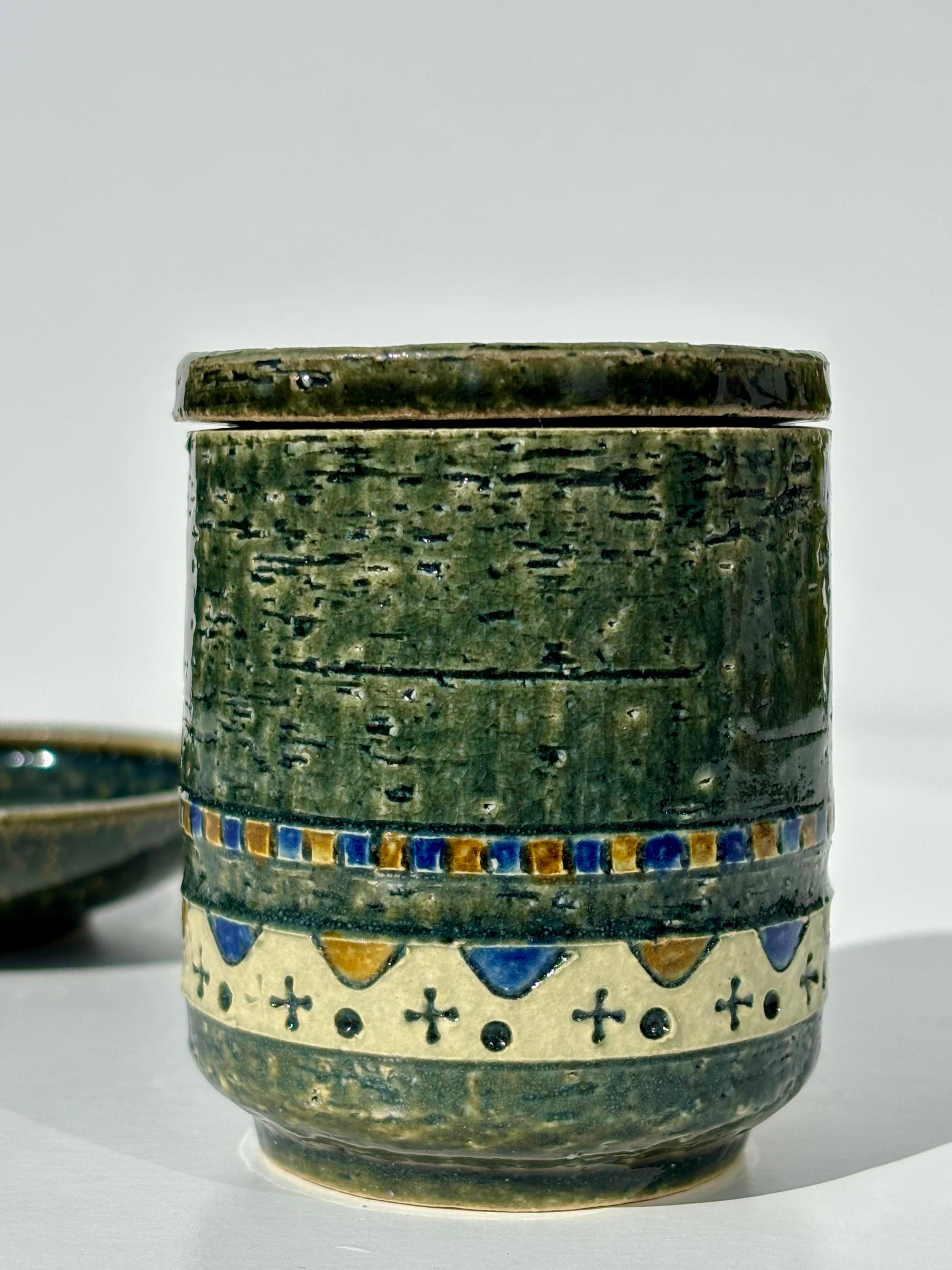 Jarre à couvercle et bol à vide-poche en grès de The Modern Scandinavian midcentury modern par Yngve Blixt pour Höganäs Sweden. Glaçure vert olive profond sur argile chamottée à décor délicat jaune crème, ocre et bleu.
Signé par l'artiste sous la