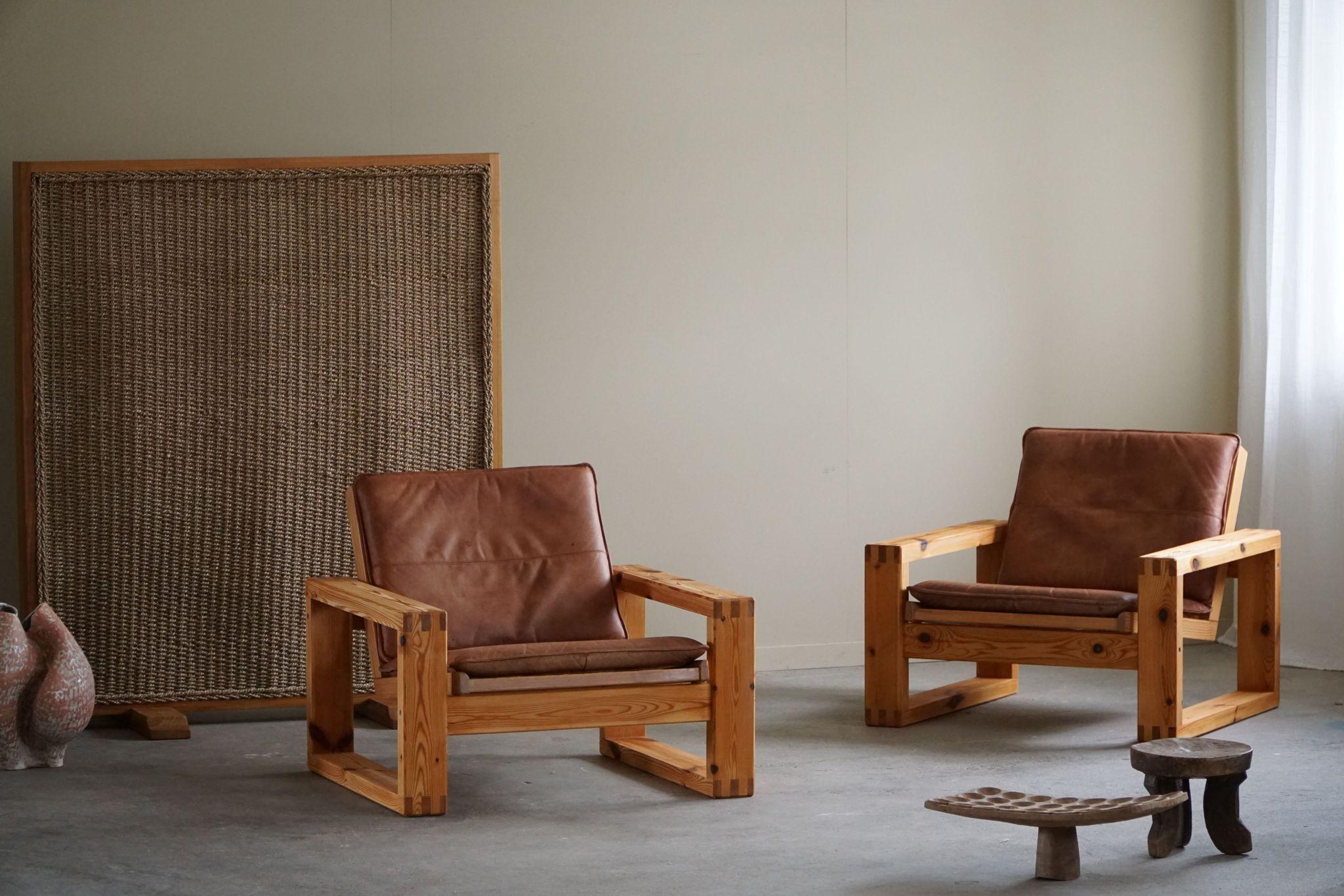 Cette paire de chaises de salon Mid-Century Modern, conçue par Yngve Ekstrøm pour Swedese dans les années 1970, présente une structure en pin massif et des coussins en cuir patiné. Le design cubiste voit dans les lignes épurées et les formes