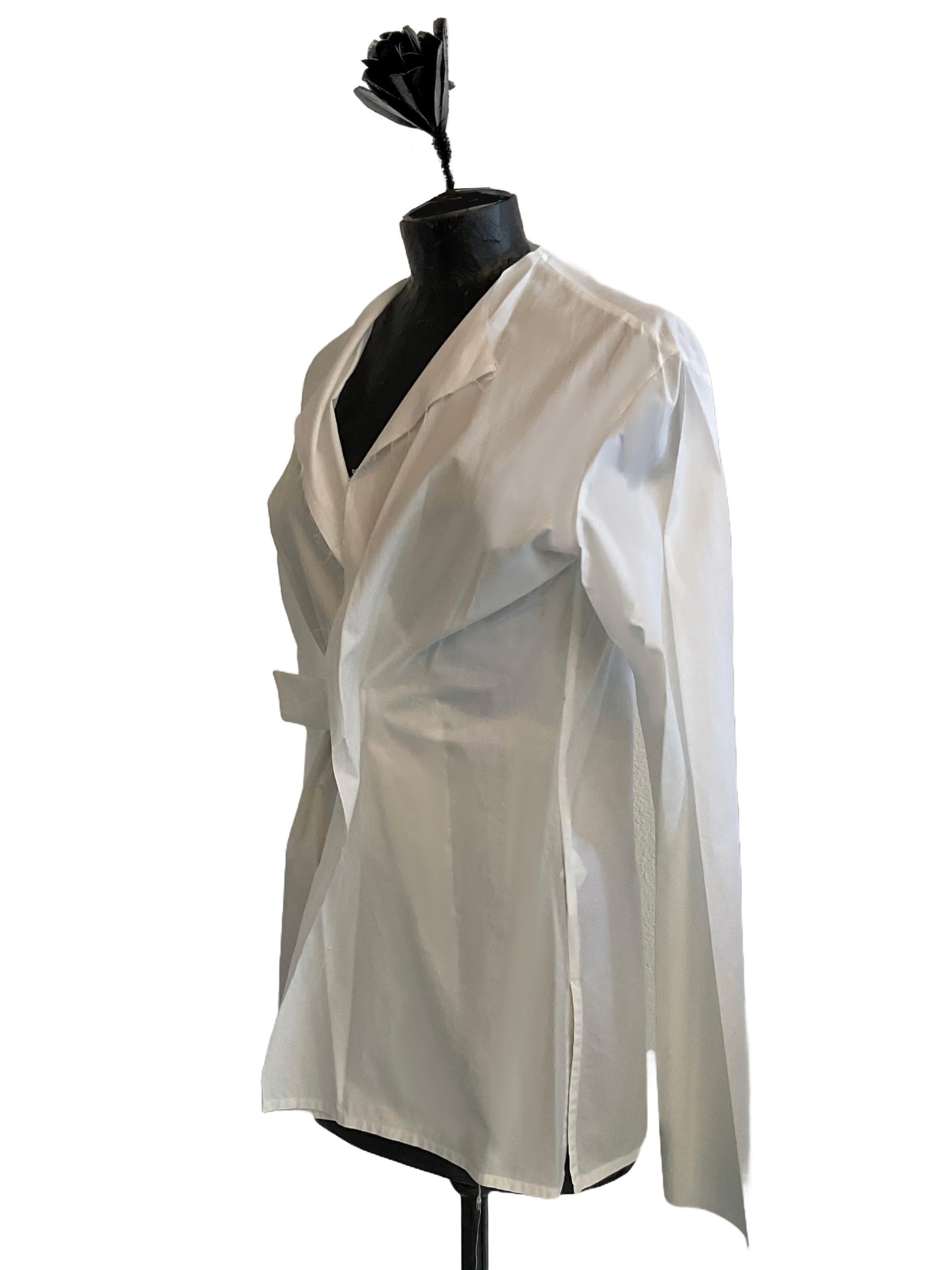 Camicia di cotone  with self-locking buckle closure by Yohji Yamamoto from the early 2000s. The shirt is collarless and partly finished raw cut. It stays tighter to the body at the front and softer at the back. The buckle is positioned at waist