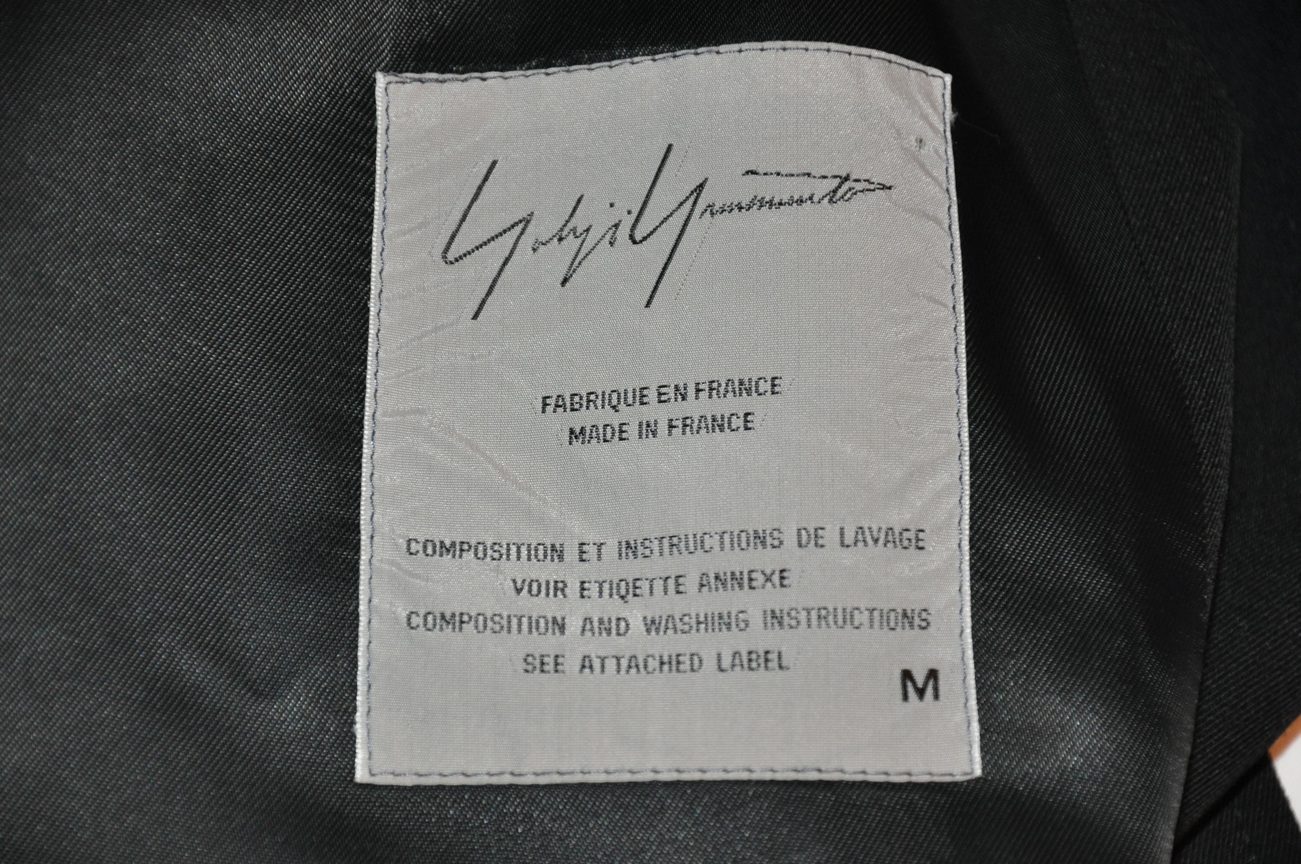      Le trench-coat déconstruit en laine brossée noire merveilleusement drapée de Yohji Yamamoto présente une poche cachée à l'intérieur, près de l'ourlet. La longueur mesure 33 pouces, les épaules mesurent 20 pouces, le cou jusqu'à la manchette est