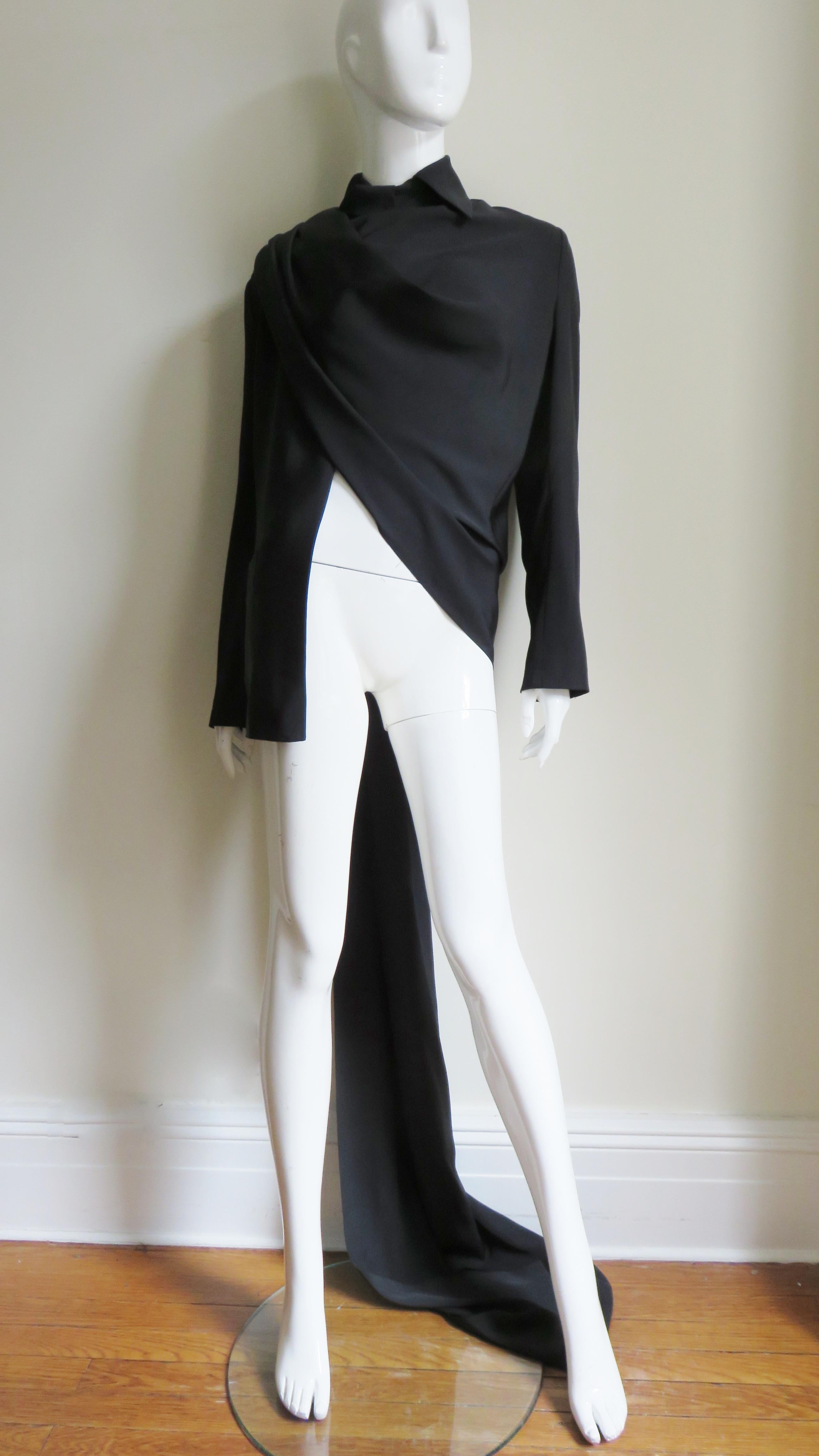 A fabulous jacket/shirt in black silk by Yohji Yamamoto.  It has a shirt collar which closes with a front button tab at the neck, long sleeves with 2 button cuffs and a pocket on one front hip.  It has an incredible long drape extending from one the
