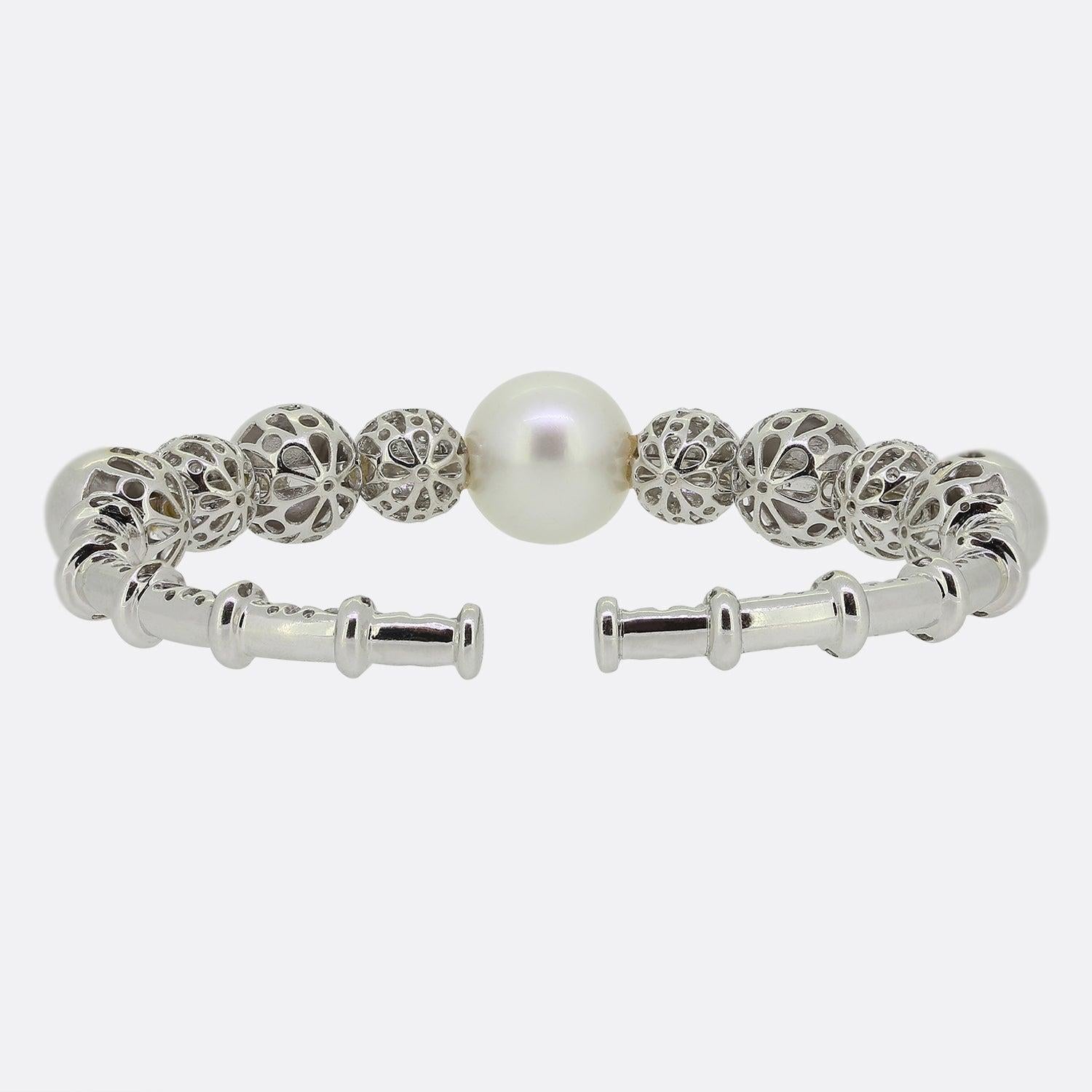 This is an 18ct white gold bangle from Yoko London. This elegant piece features a large lustrous South Sea pearl offset by four white gold spheres on either side. These spherical motifs alternate between a plain polished finished and being pave set
