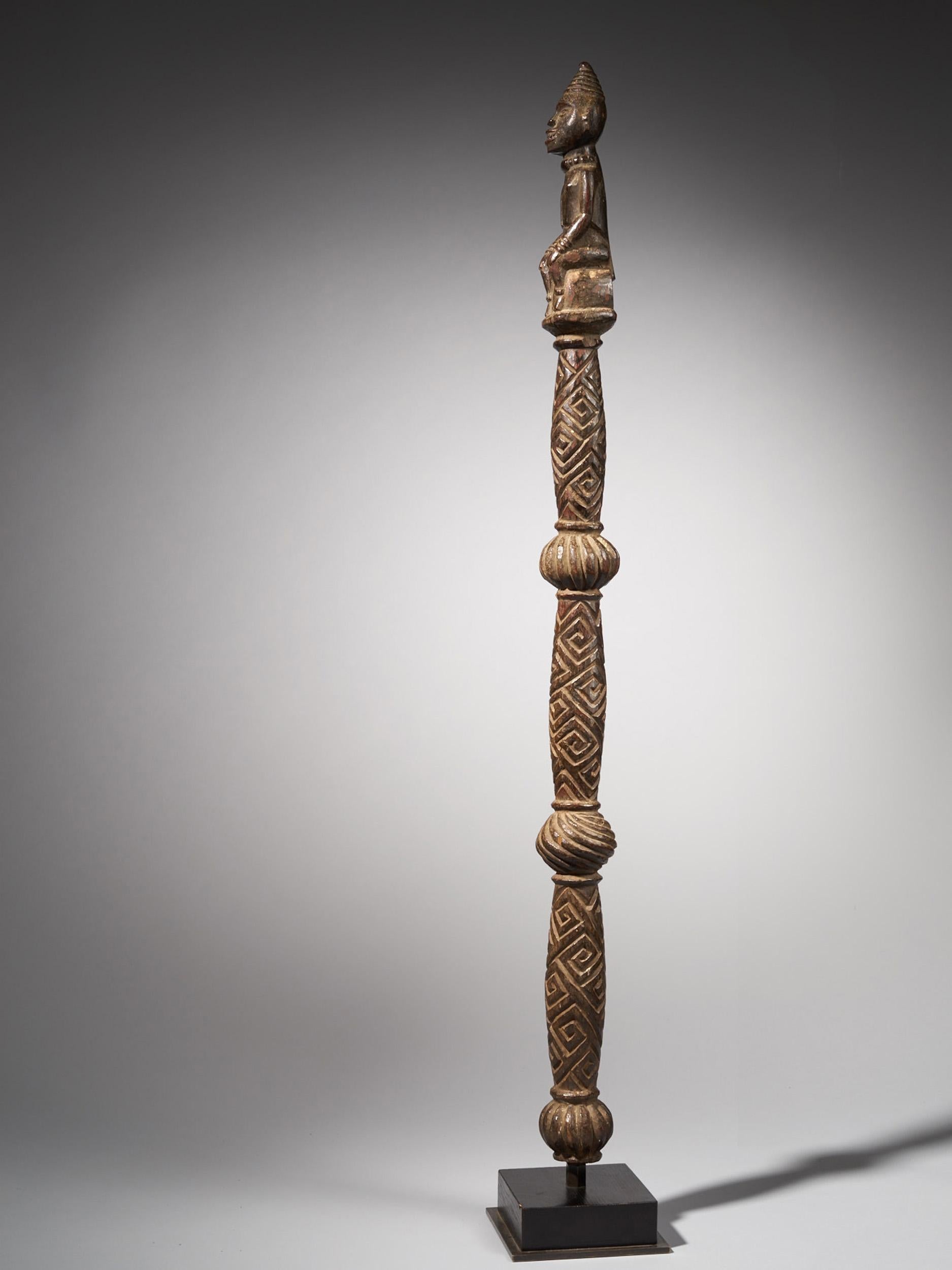 A Wooden Yombe Mwaala Chief Staff, with three globular elements. The Finial is a finely carved female figure kneeling, the hands resting on the knees and with raised scarification marks above the prominent breasts. The head carved powerfully with