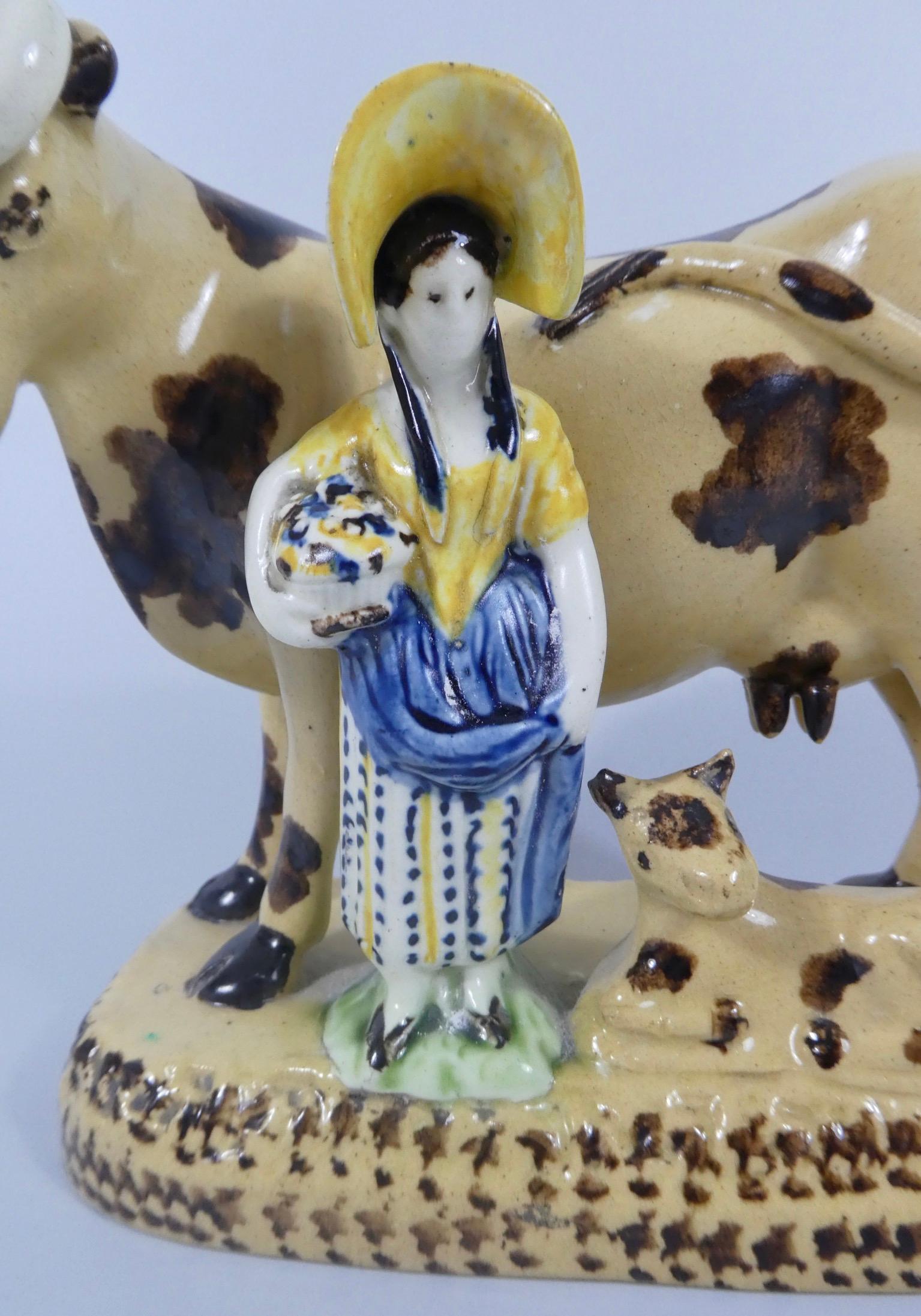 Yorkshire pottery Prattware group, circa 1820. Modelled as a shepherdess, holding a basket,and stood with a cow and its calf. The shepherdess, decorated in Pratt coloured glazes, whilst the cow and the calf, are decorated with brown spits, on a buff
