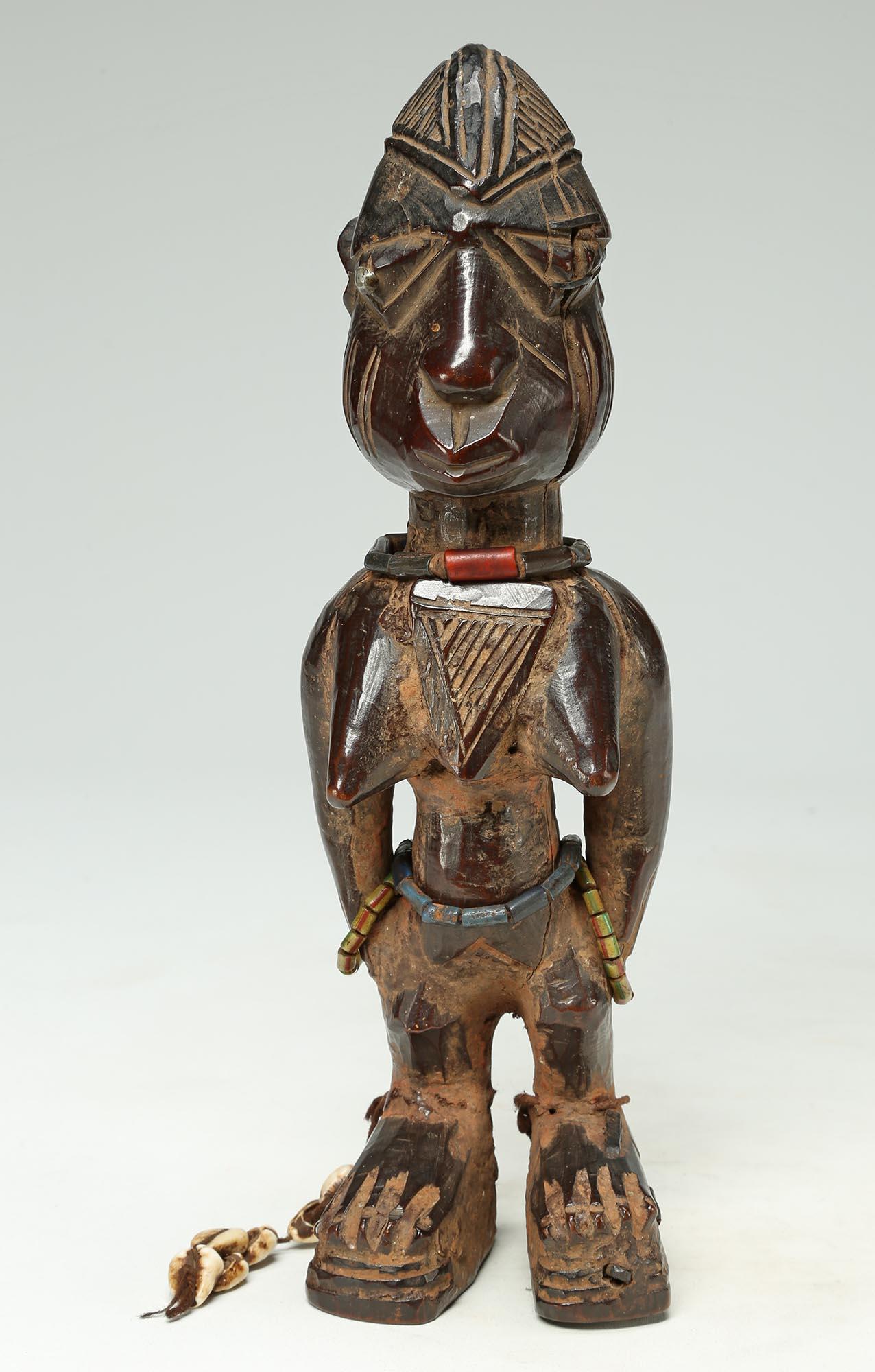 A finely carved female twin figure, ere Ibeji, Yoruba People, Nigeria, created in the early 20th century. 
With a domed plaited coiffure, expressive eyes, and extensive wear and polish from native use. Areas of encrusted red camwood powder between