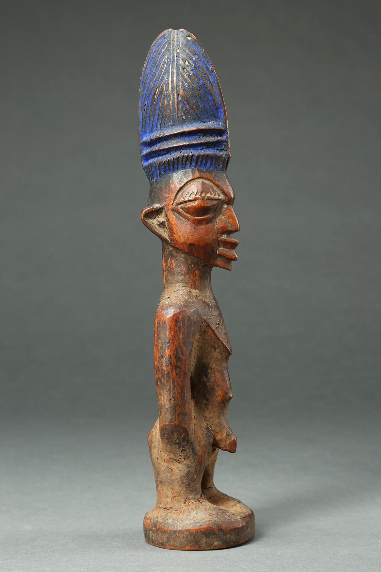 A finely carved male twin figure, ere Ibeji, Yoruba People, Nigeria, created in the early 20th century. 
With a tall plaited coiffure, expressive eyes, and extensive wear and polish from native use. Areas of encrusted camwood powder between arms and